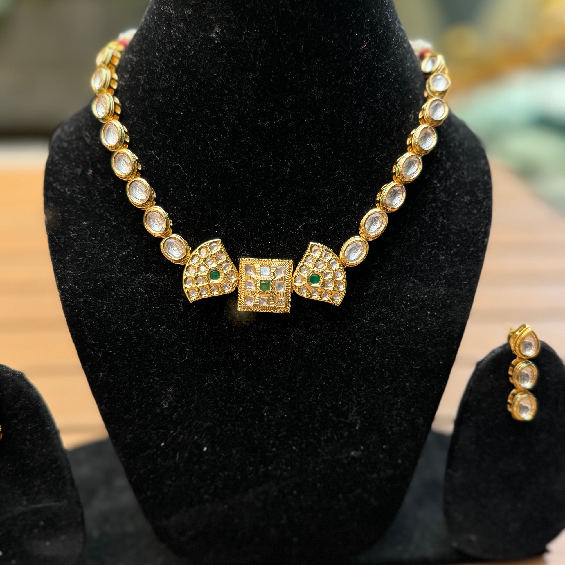 A double-sided Kundan necklace with intricate handcrafted designs and stunning Kundan stones displayed on a black stand.
