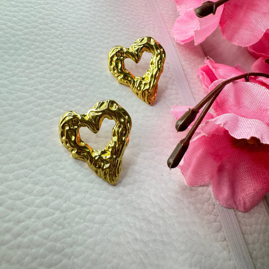 Gold earrings on a textured white surface with pink flowers in the background