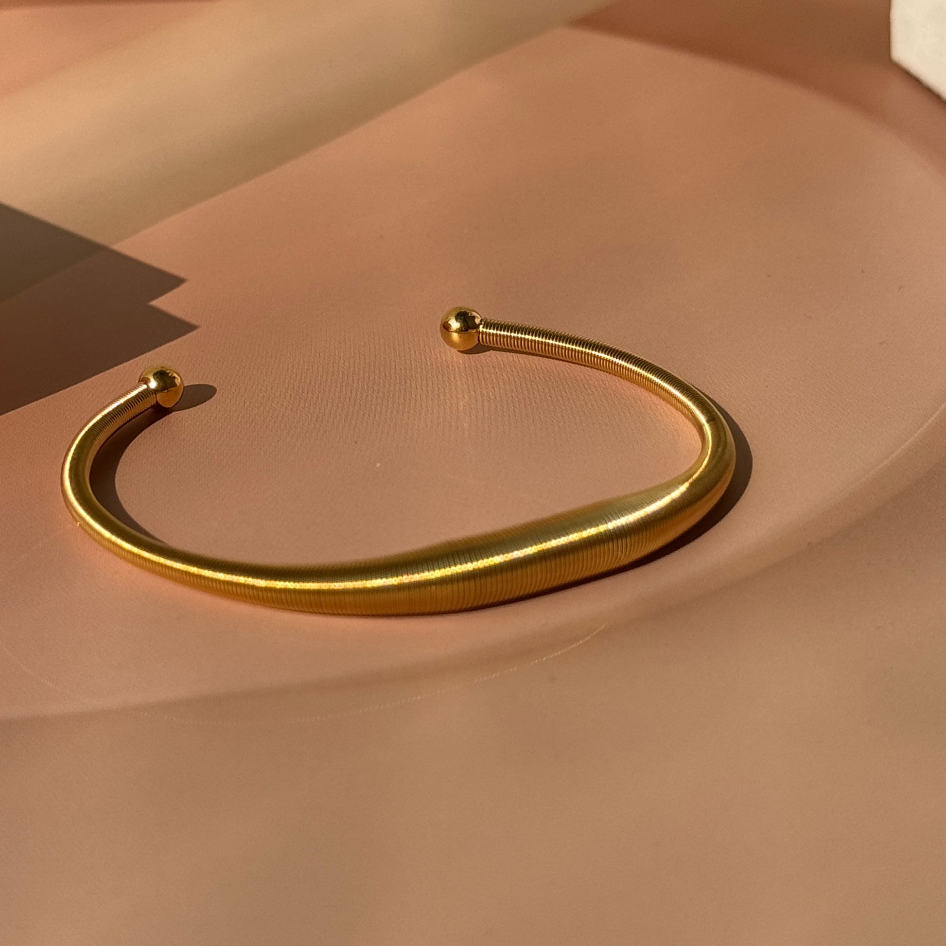 A gold-colored spiral open hand cuff bracelet on a beige surface.