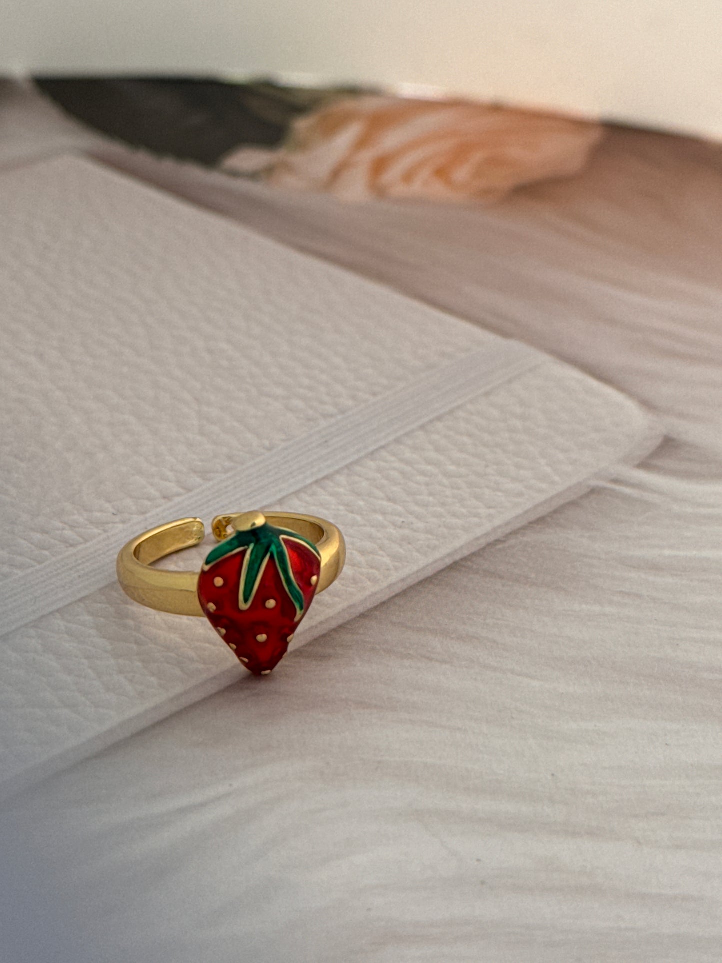 Gold ring with strawberry design on a textured white surface