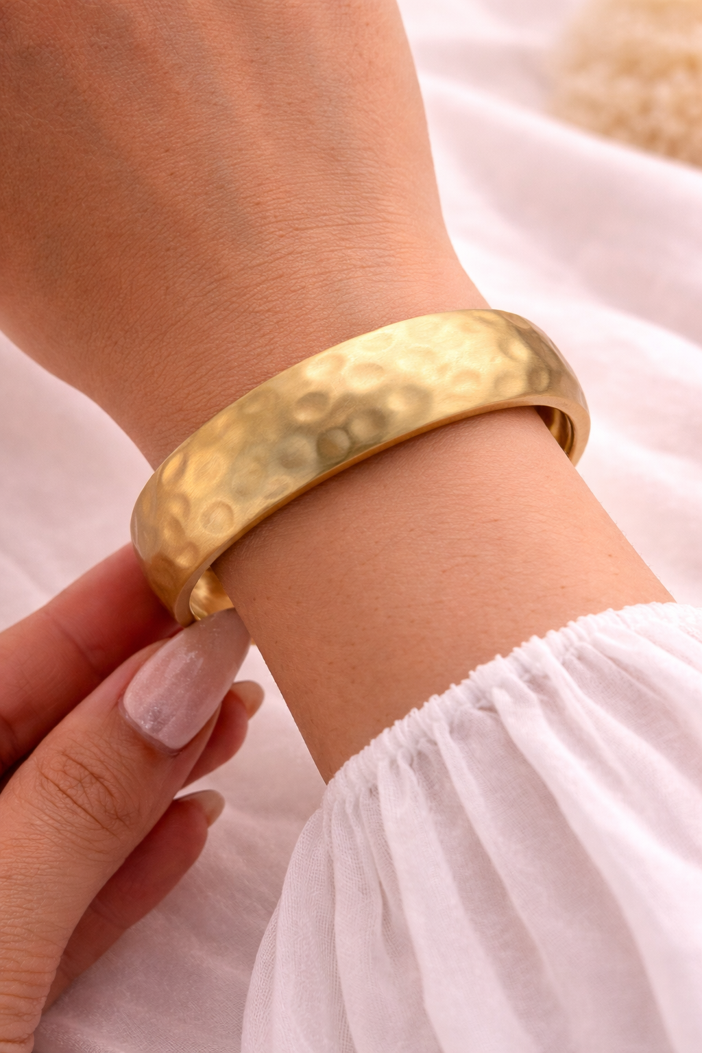Gold bracelet on a wrist with a soft white background