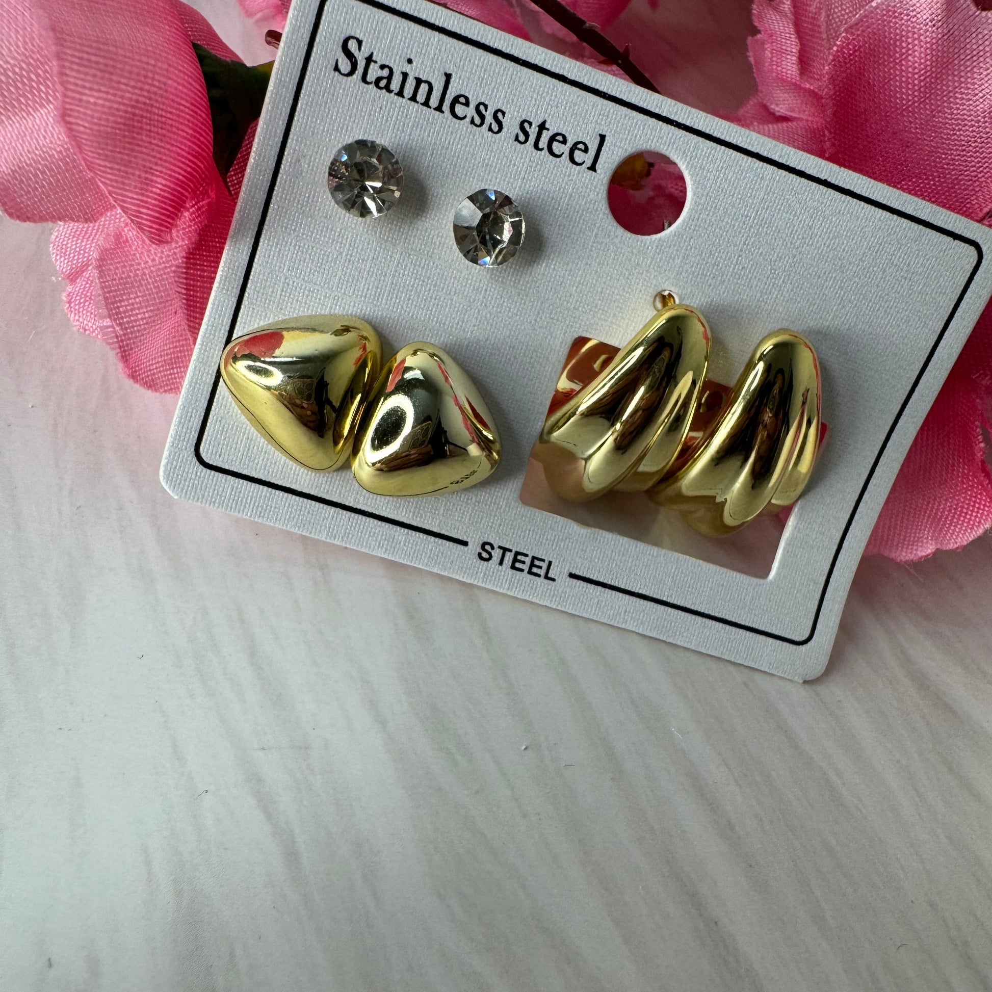 Three sets of anti-tarnish studs in gold color, presented on a card, with a pink floral background.