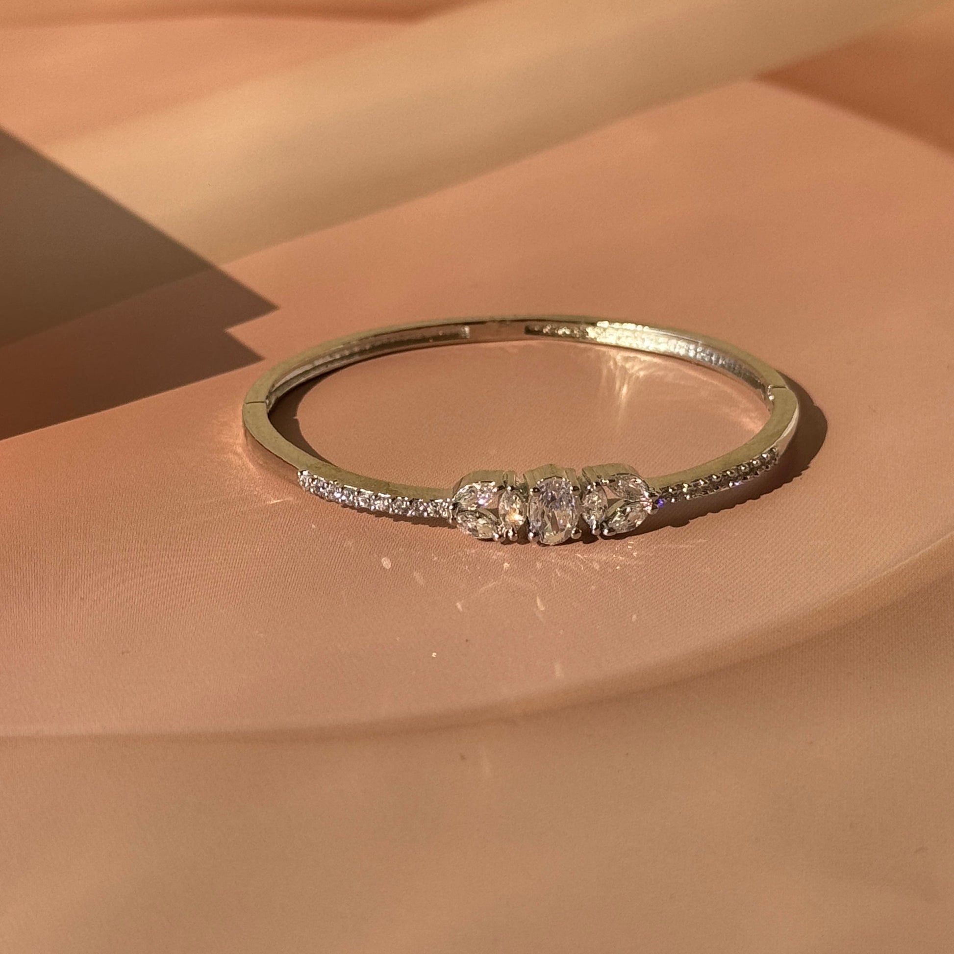 A gold-colored bracelet with sparkling stones set in a row, displayed against a pink background.