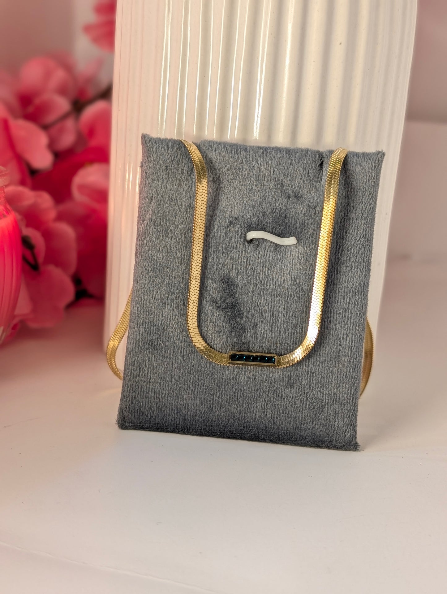 Gray pouch with gold zipper on a white surface with pink flowers in the background