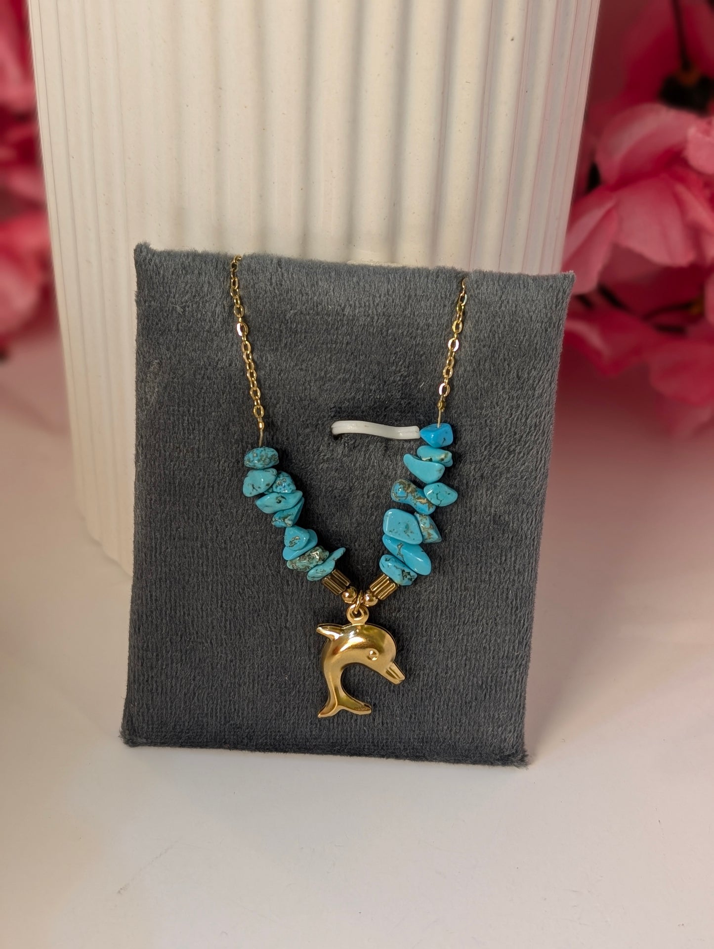 Necklace with turquoise beads and gold dolphin charm on a gray display card.