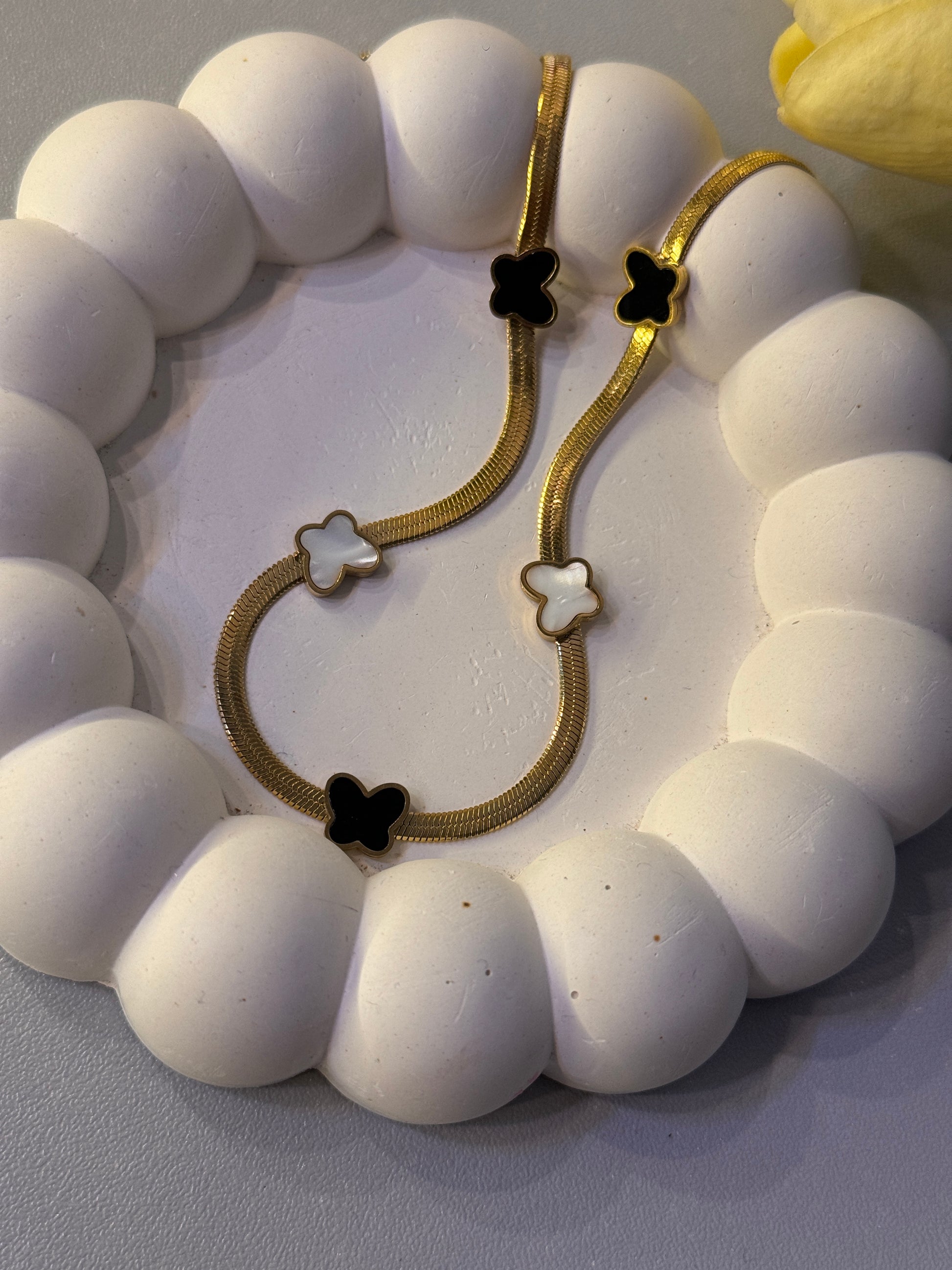 Gold bracelet with black and white flower charms on a white stone surface