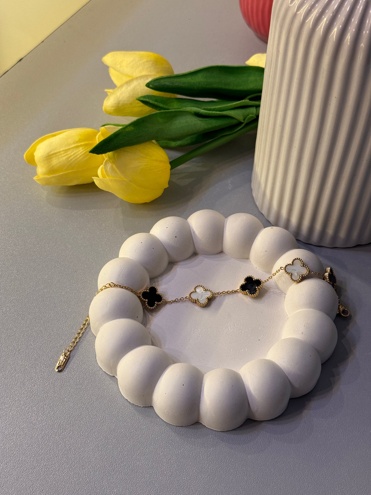 White beaded bracelet with gold accents on a light gray surface, next to yellow tulips.