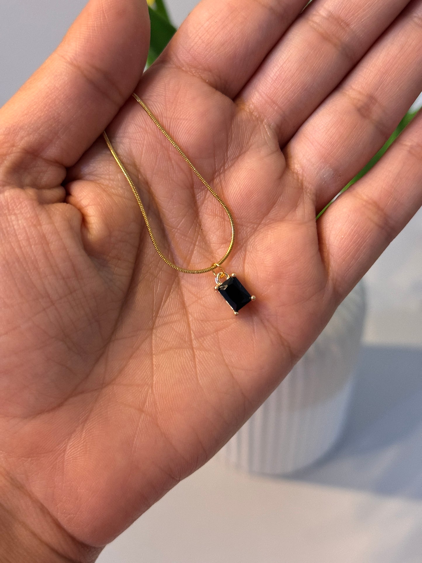 Gold necklace with a black pendant held in a hand against a blurred background