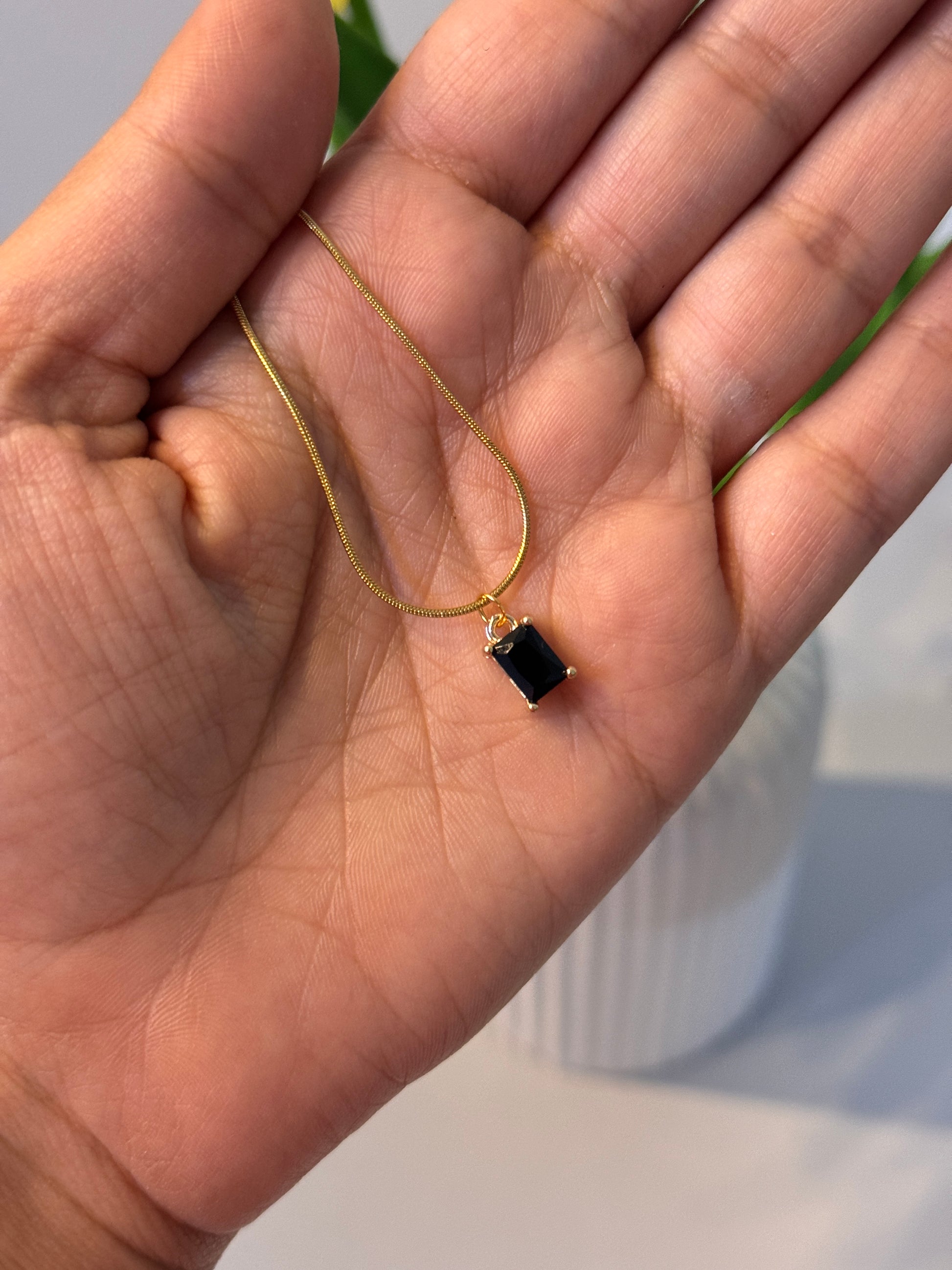 Gold necklace with a black pendant held in a hand against a blurred background