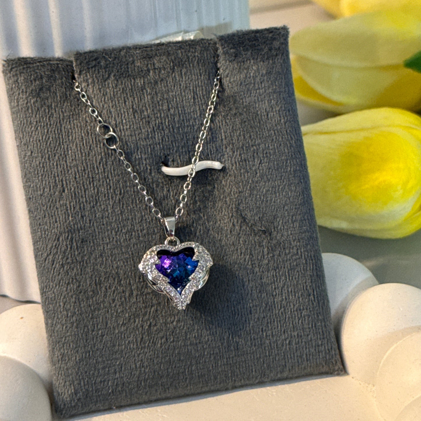 Necklace with a heart-shaped purple gemstone on a gray card with yellow tulips in the background