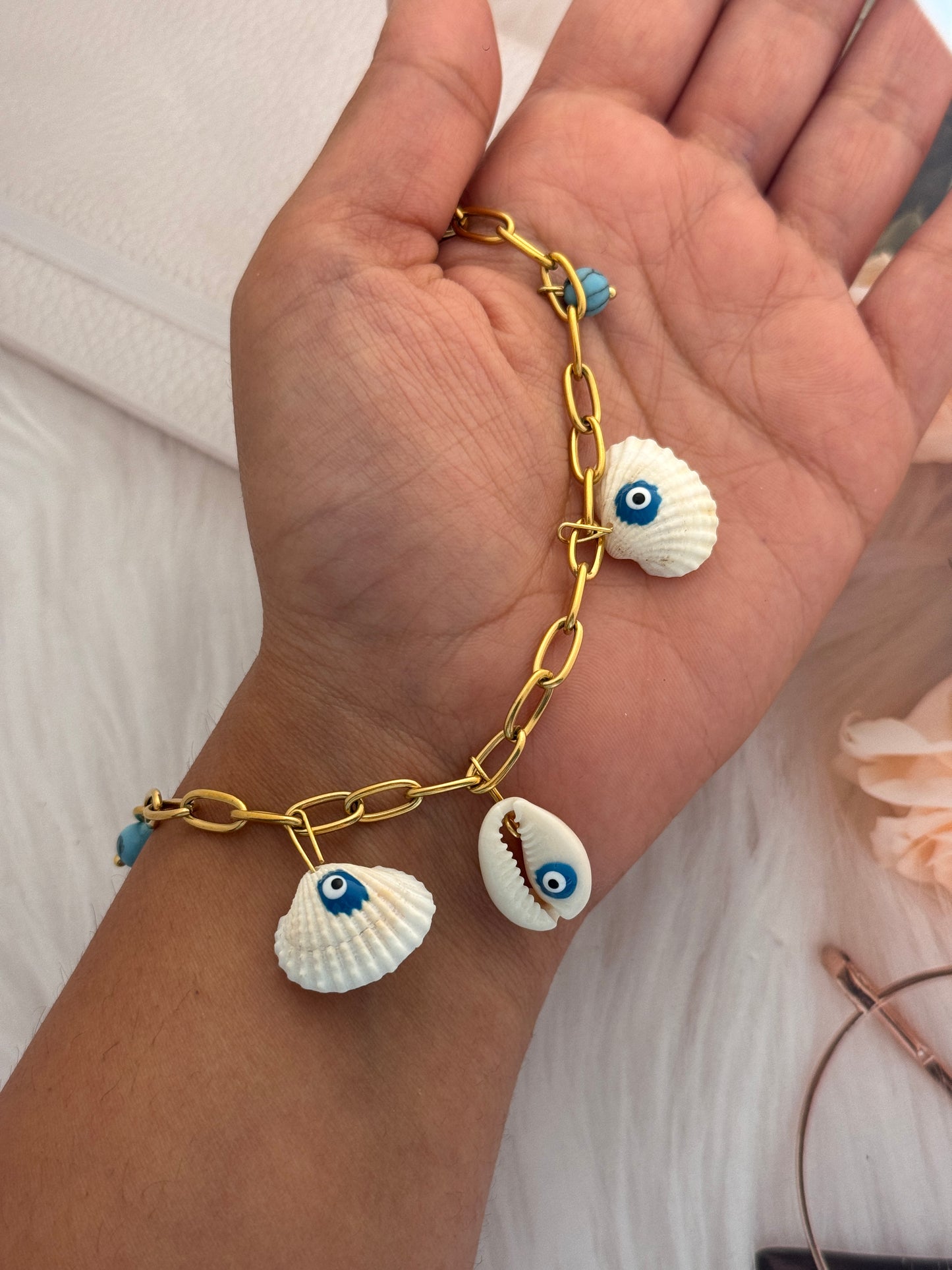 Gold bracelet with shell charms on a wrist against a neutral background