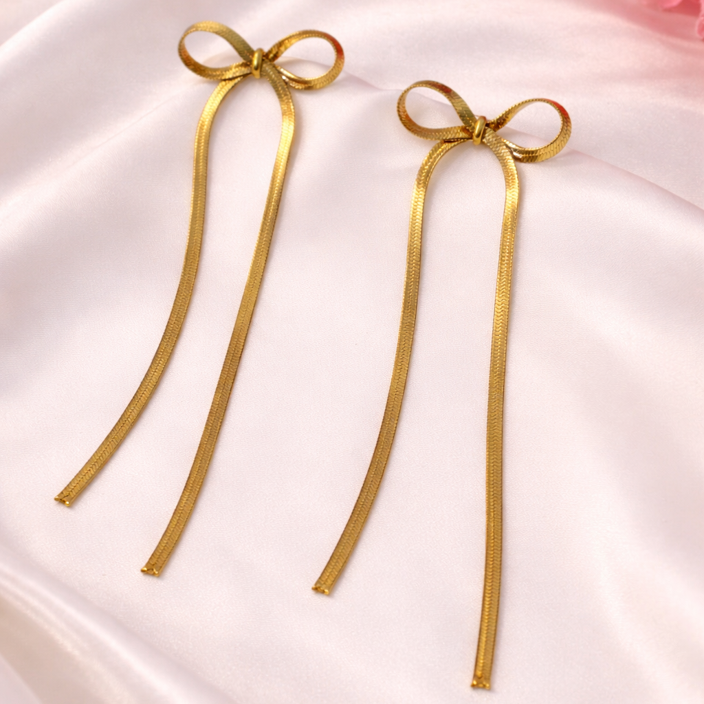 Gold bow-shaped earrings on a pink satin background