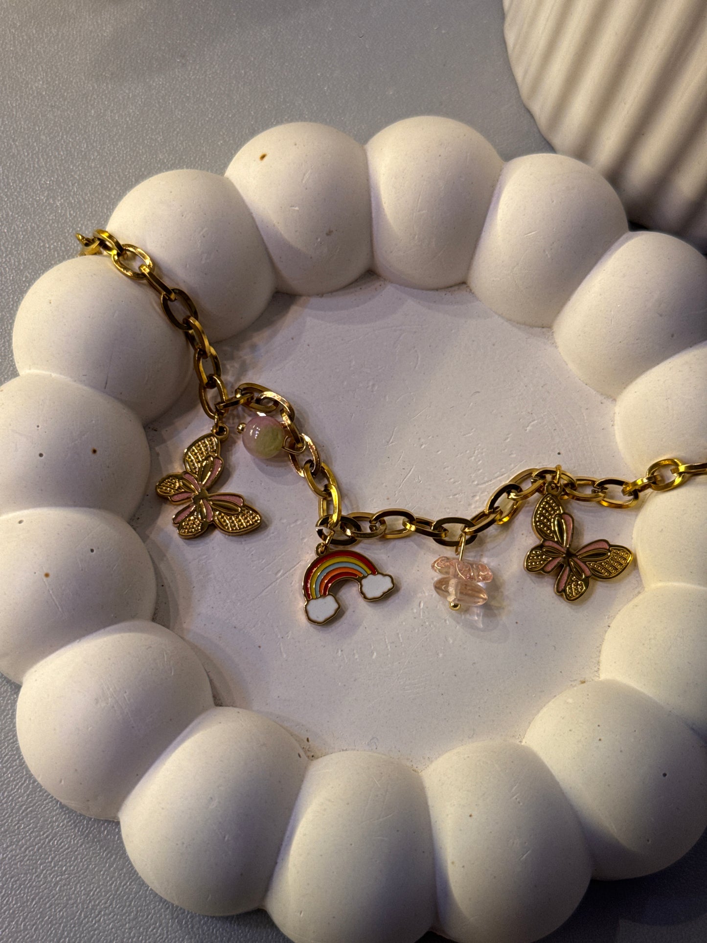 White beaded bracelet with gold charms on a white dish