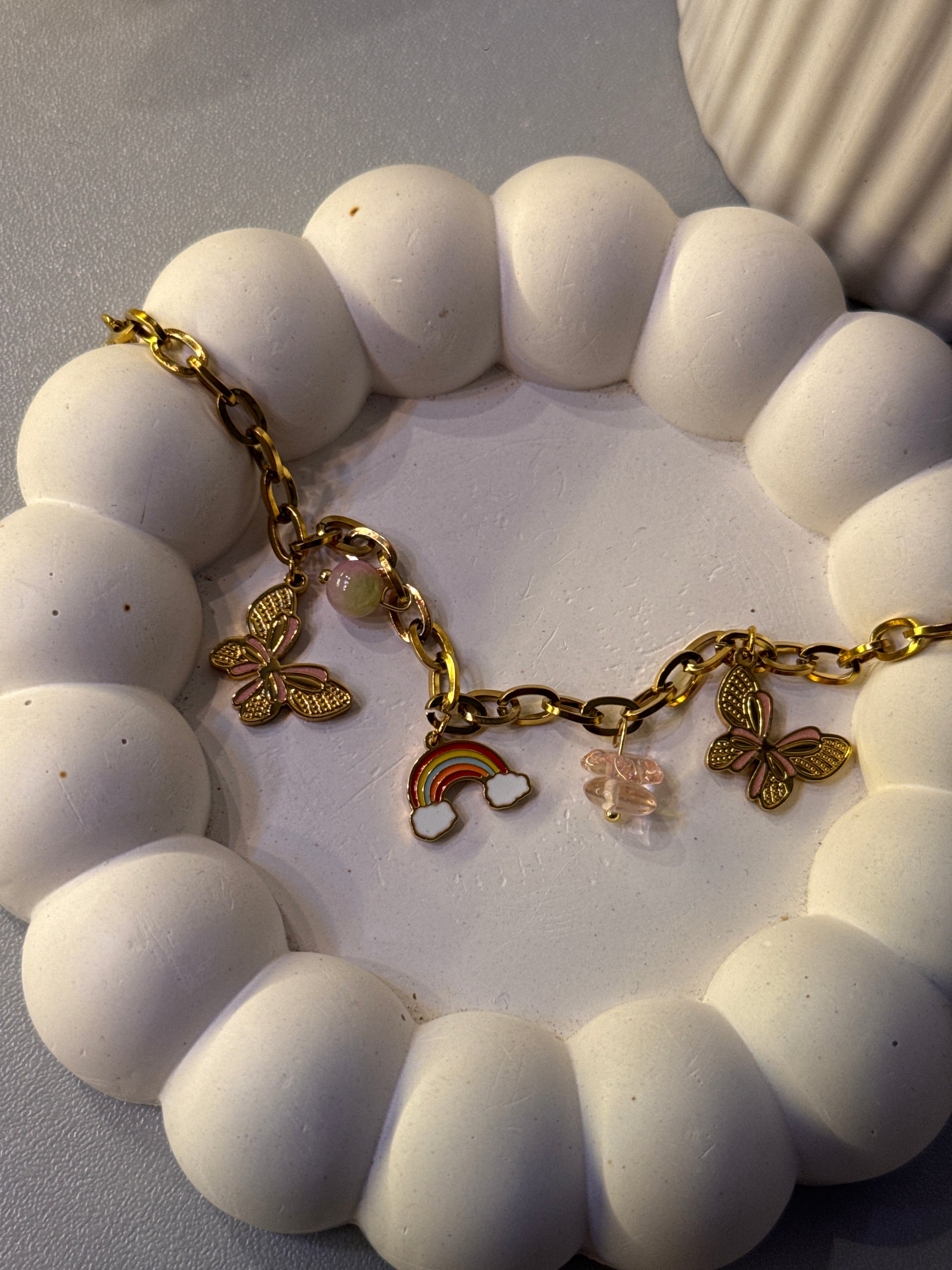White beaded bracelet with gold charms on a white dish