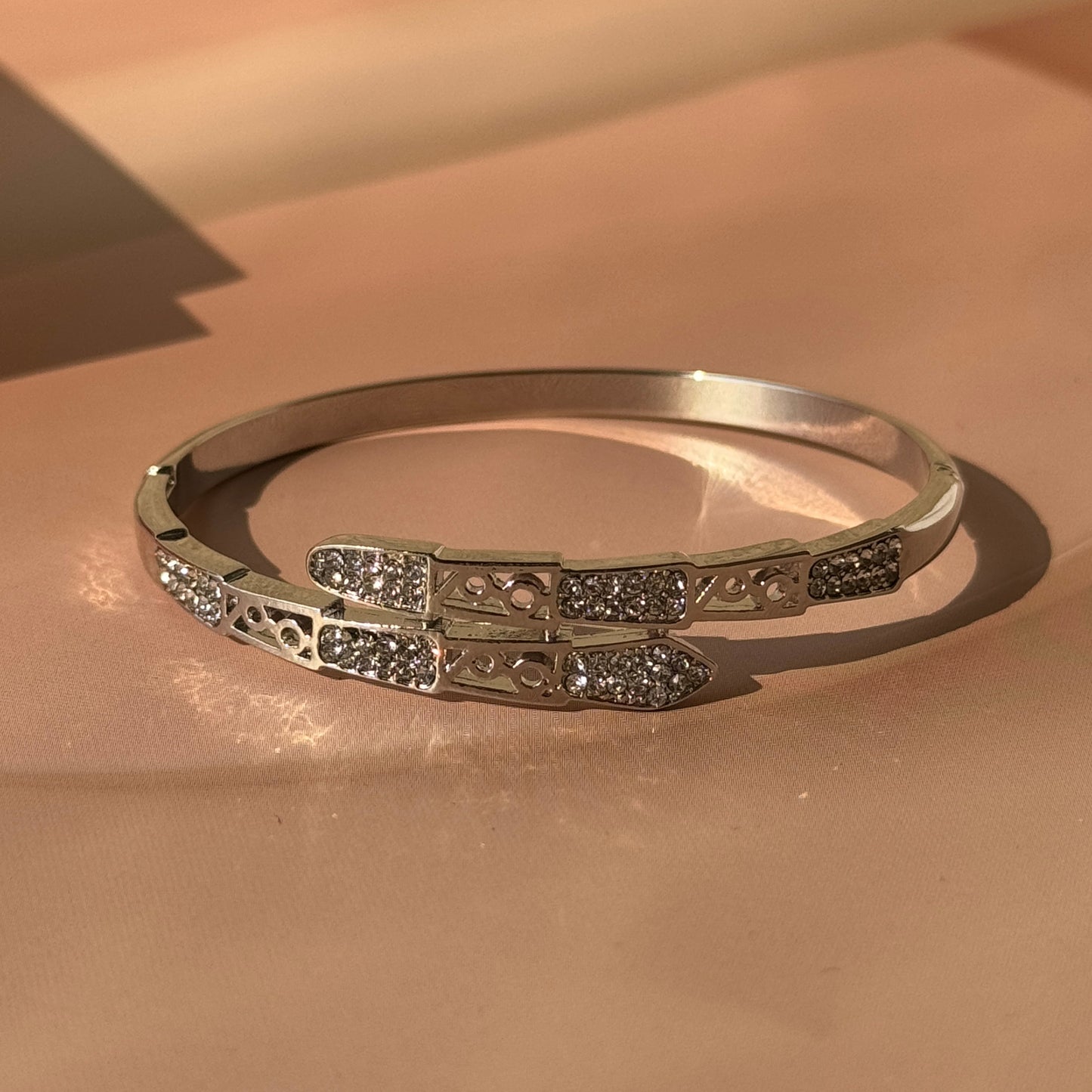 A silver bracelet with intricate designs and embellishments, displayed against a pink background.