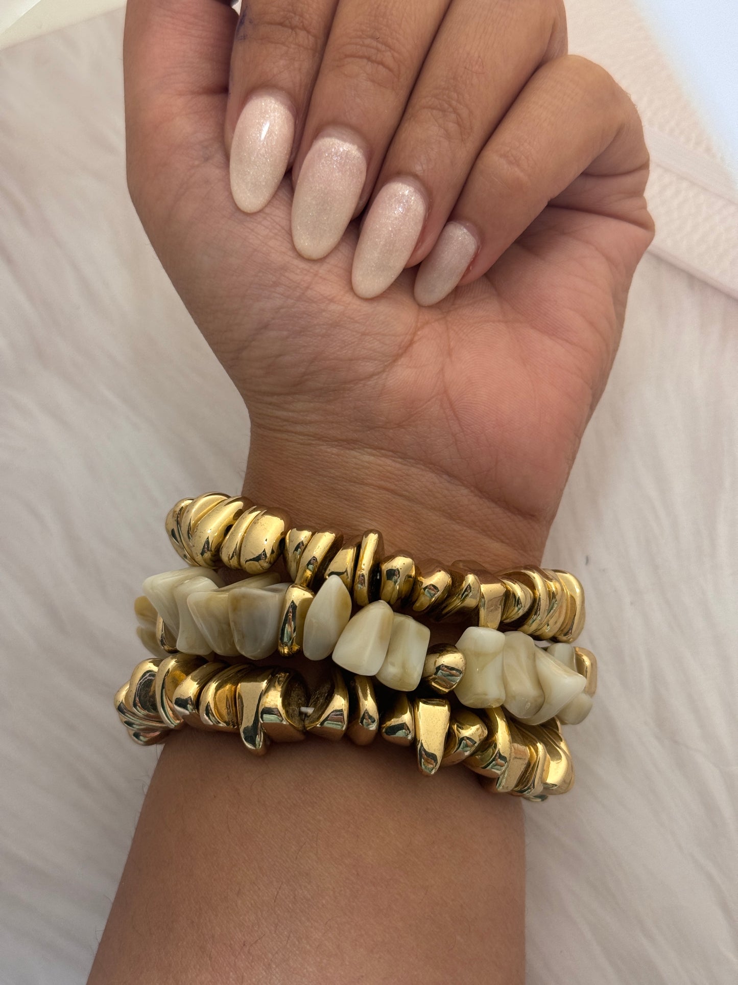 Gold and bone-patterned bracelets on a wrist against a neutral background