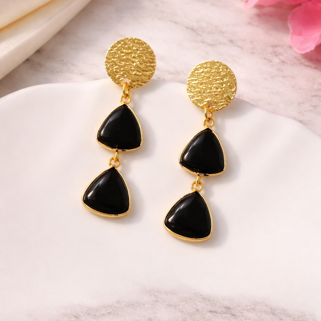 Gold and black earrings on a marble surface with pink flowers in the background