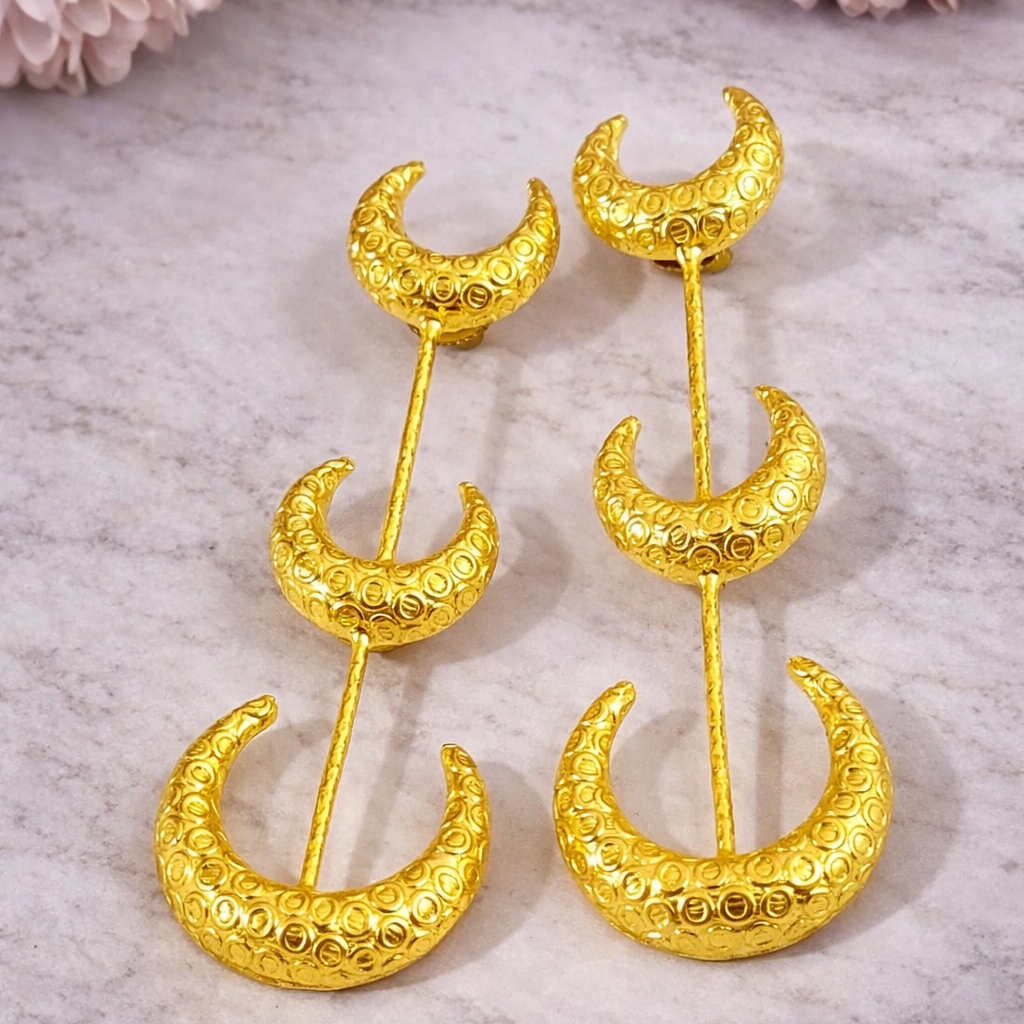 Gold moon-shaped earrings on a marble surface with pink flowers.
