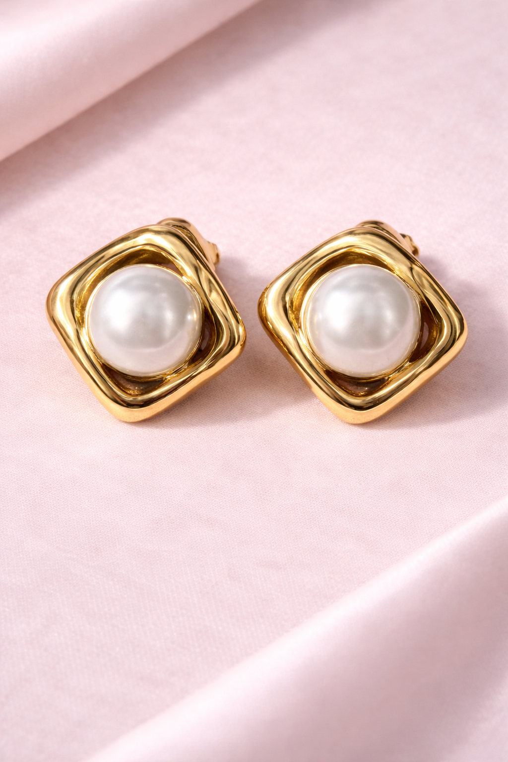 Gold earrings with pearl-like stones on a pink background
