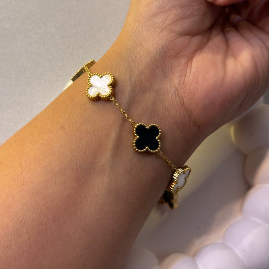 Gold bracelet with black and white clover-shaped charms on a wrist.