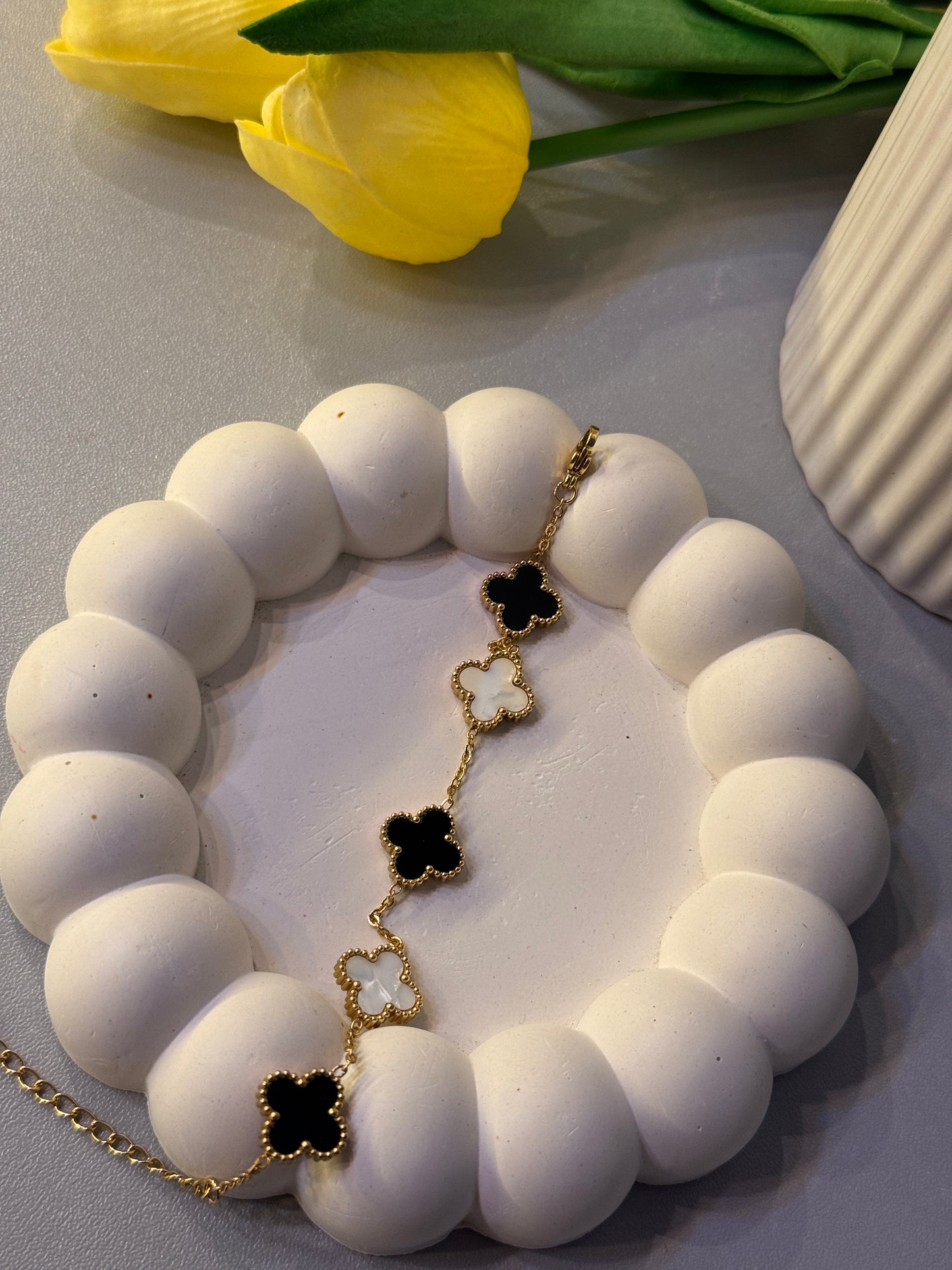 White beaded bracelet with black flower charms on a light surface with a yellow tulip and green leaves.