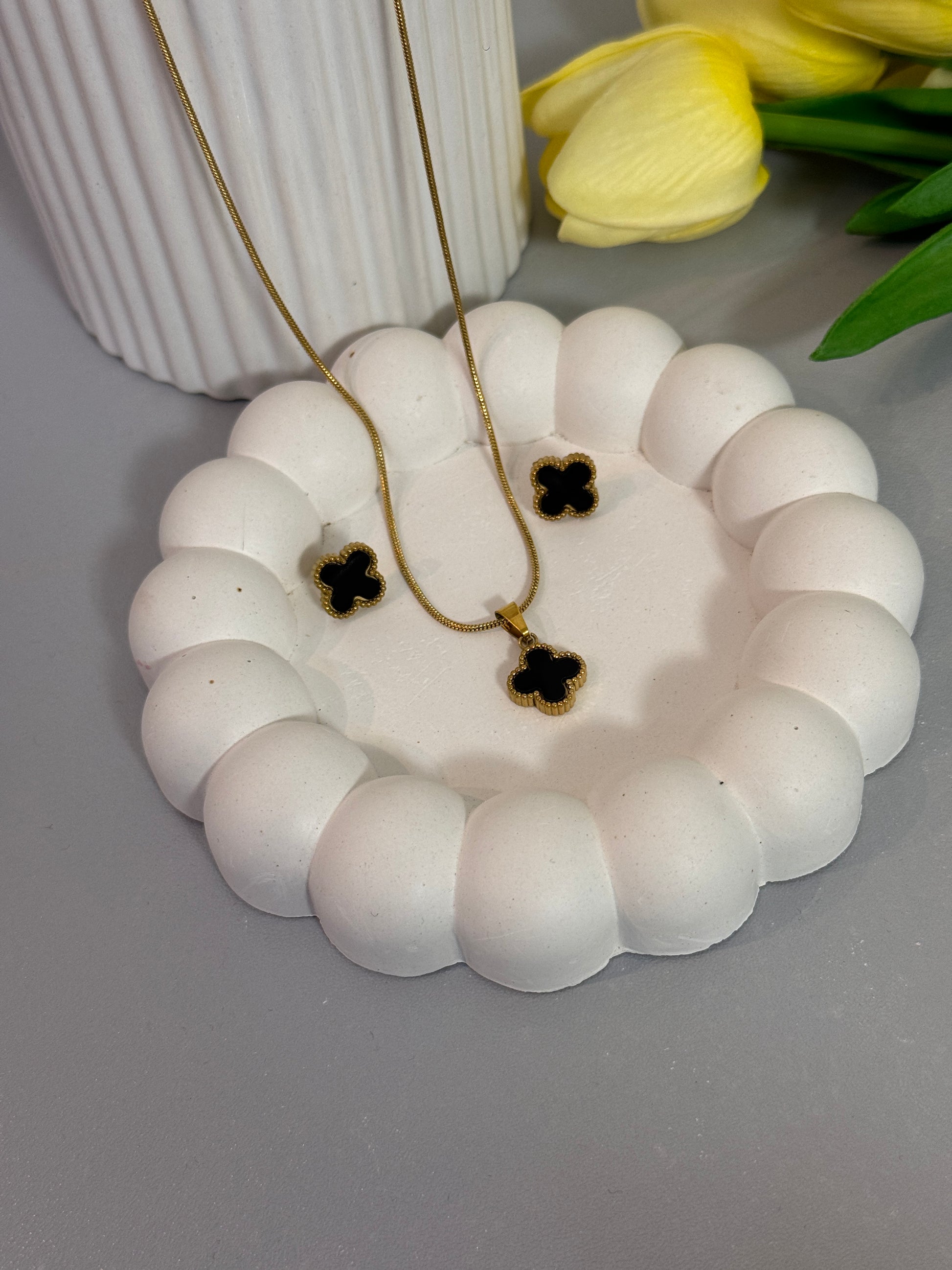 White decorative wreath with black and gold flowers on a gray surface, with yellow tulips in the background.
