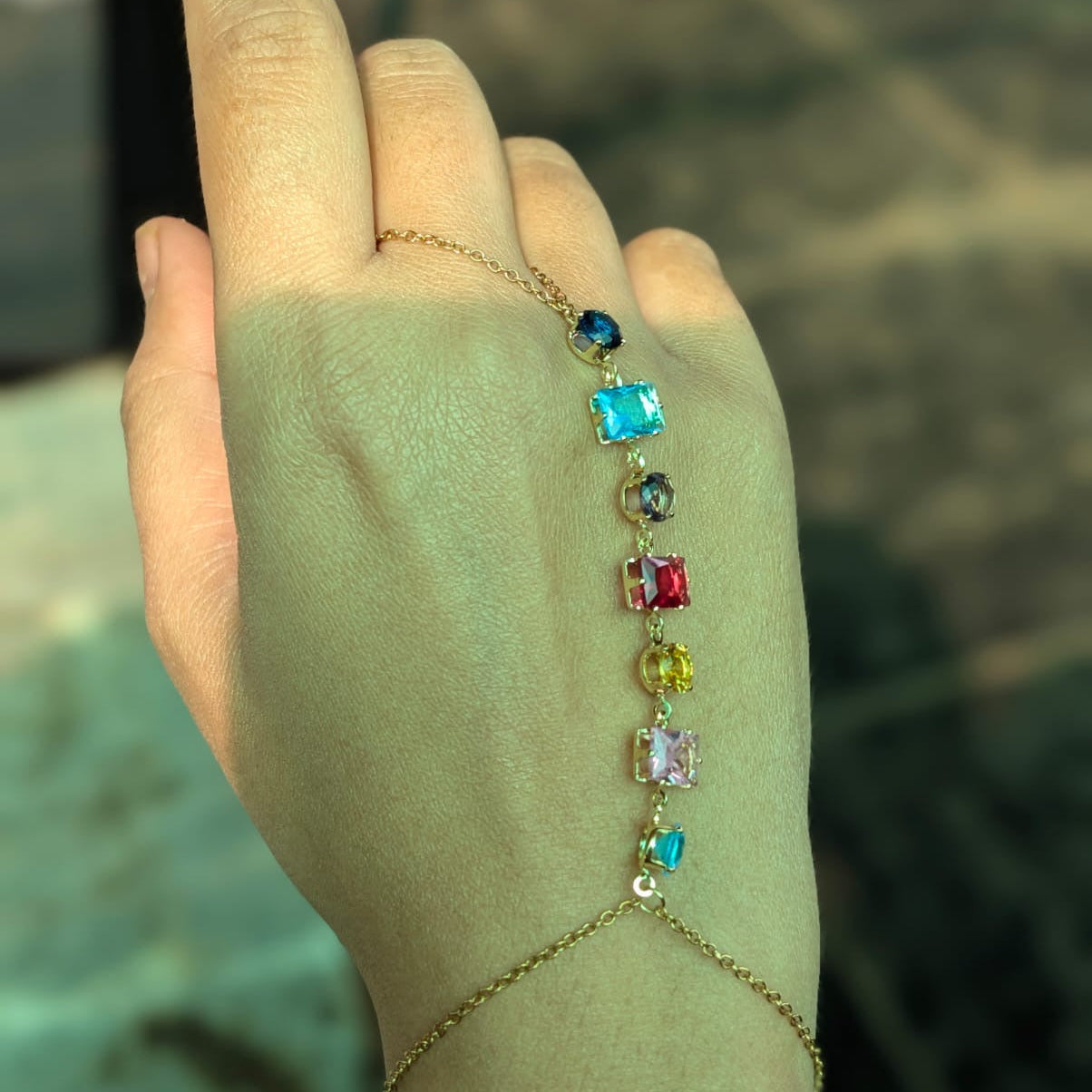 Hand wearing a bracelet with colorful gemstones against a blurred background