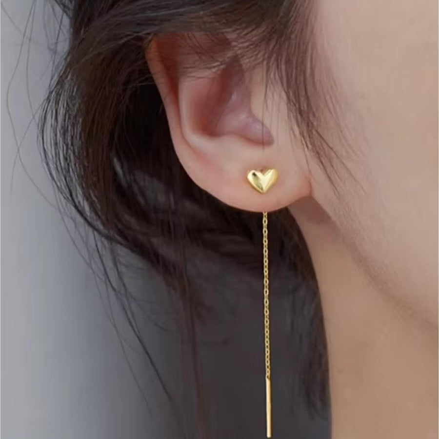 Gold heart-shaped earring worn by a person with a neutral background