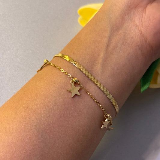 Gold bracelet with star charms on a wrist against a neutral background