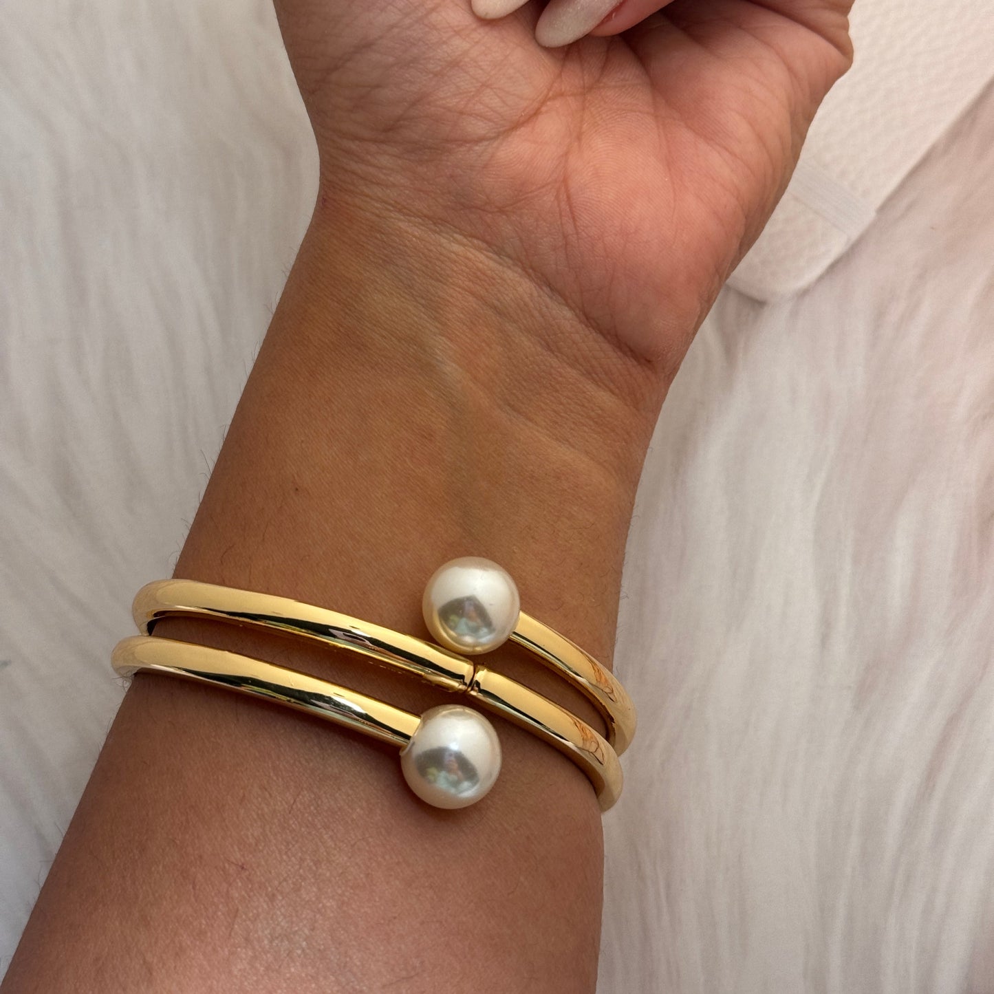 Gold bracelet with pearl accents on a wrist against a neutral background
