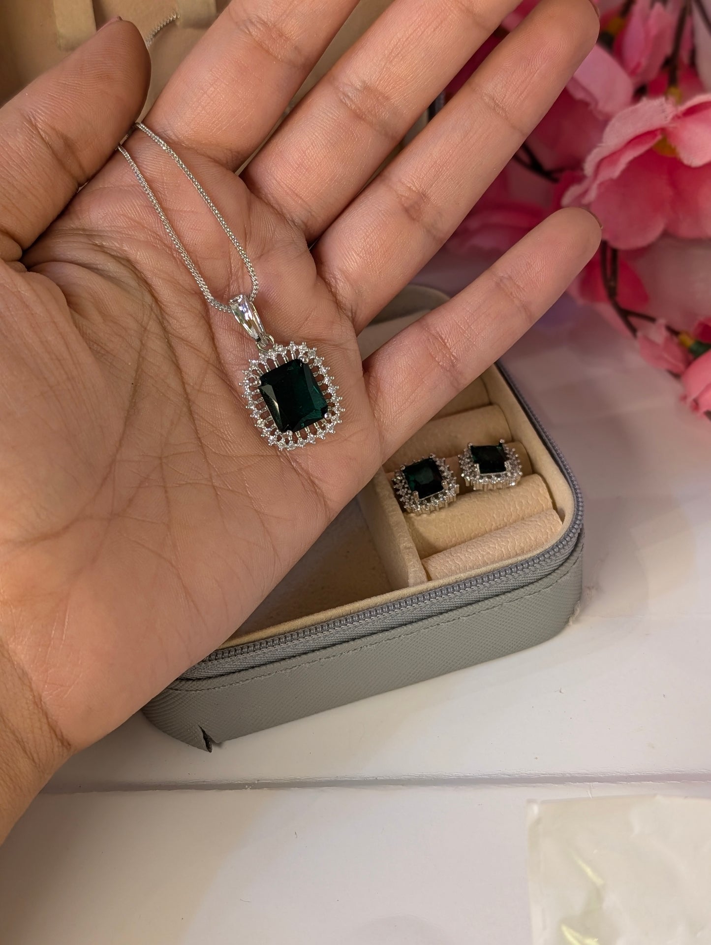 Jewelry set with pendant and earrings on a hand, with a jewelry box in the background.
