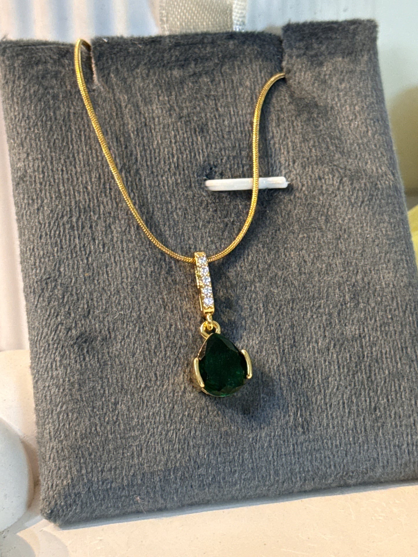 Gold necklace with a green heart pendant on a gray textured surface