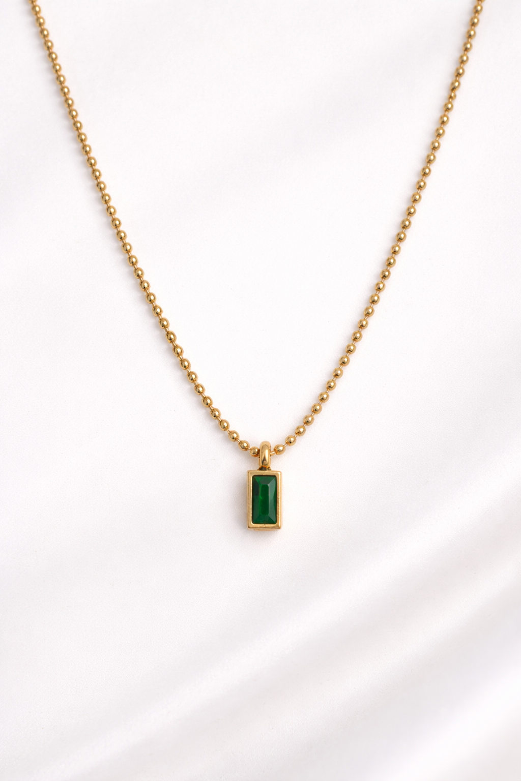Gold necklace with a green gemstone pendant on a white background