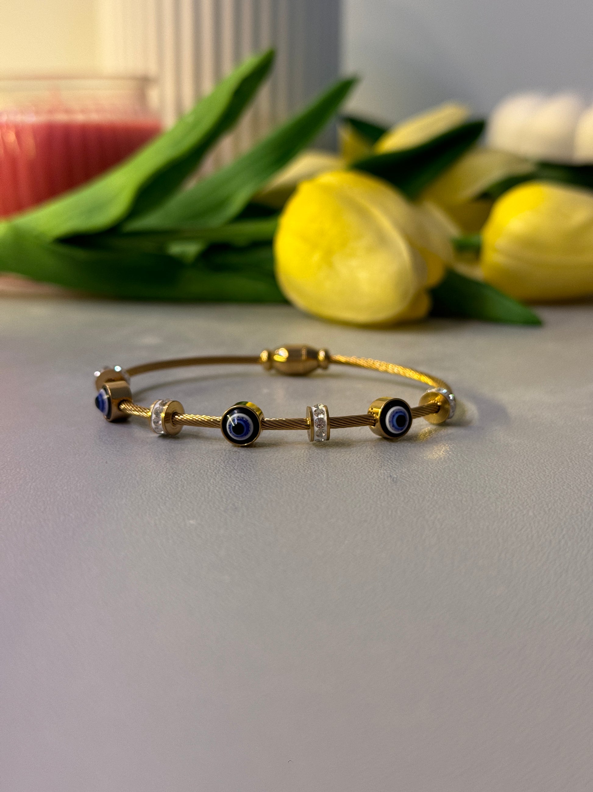 Gold bracelet with blue stones on a white surface next to yellow flowers