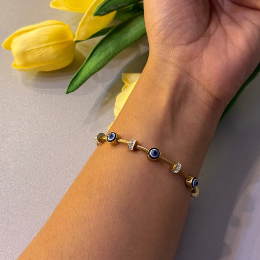 Hand wearing a gold bracelet with blue stones, holding yellow tulips against a neutral background