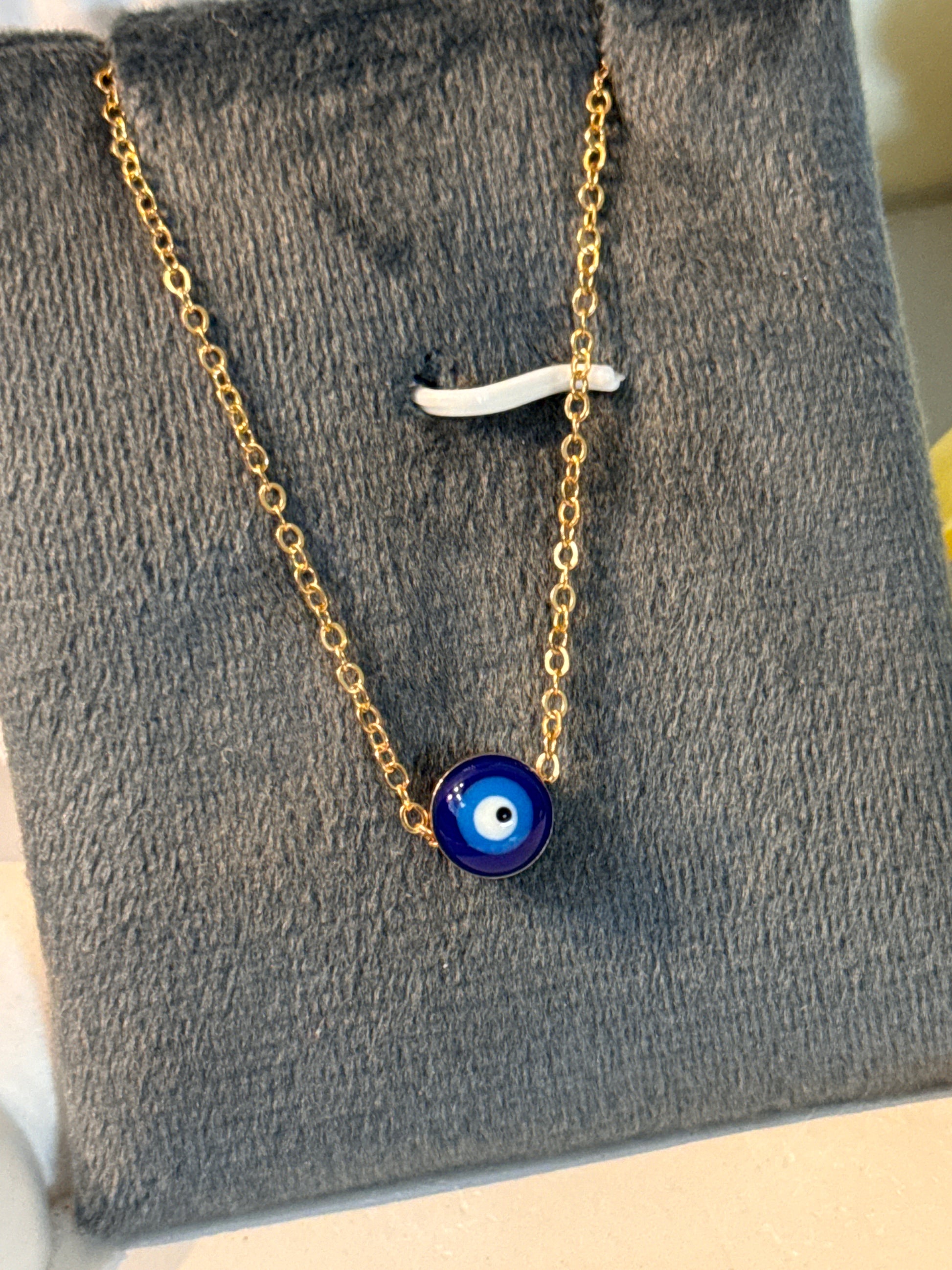 Gold chain necklace with a blue evil eye pendant on a gray textured surface.