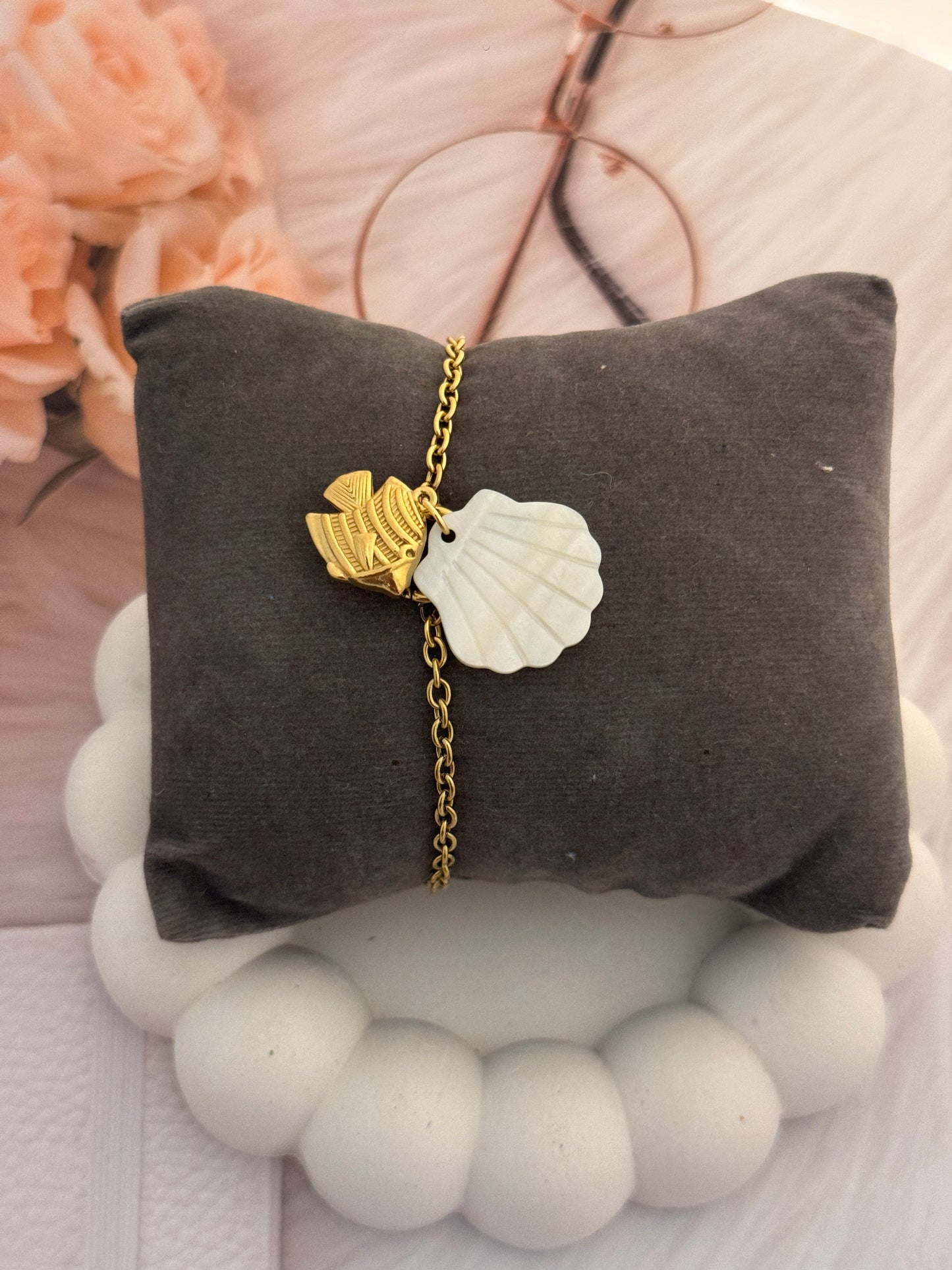 Bracelet with shell and fish charm on a gray pillow
