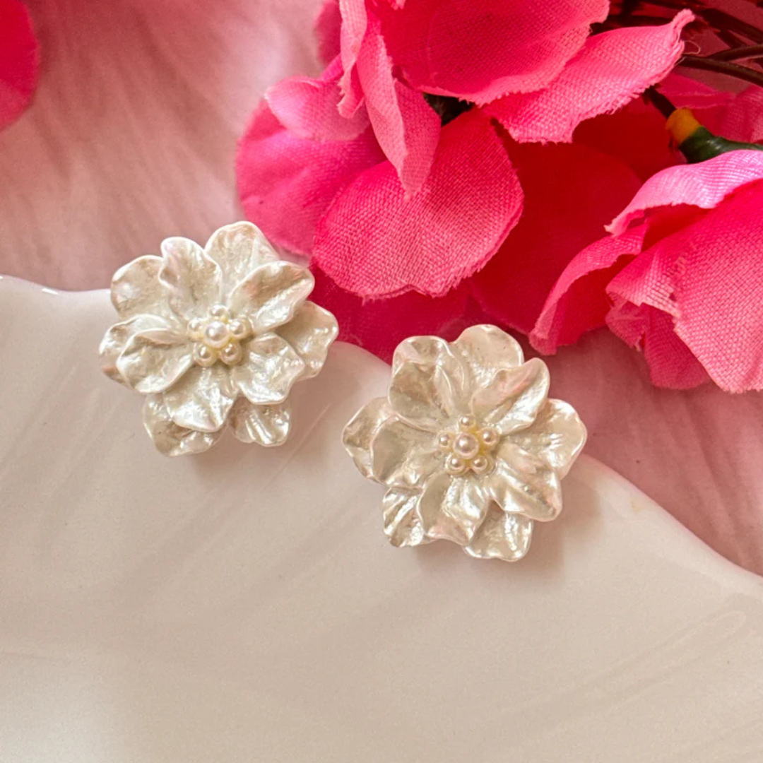 White flower-shaped earrings on a pink floral background