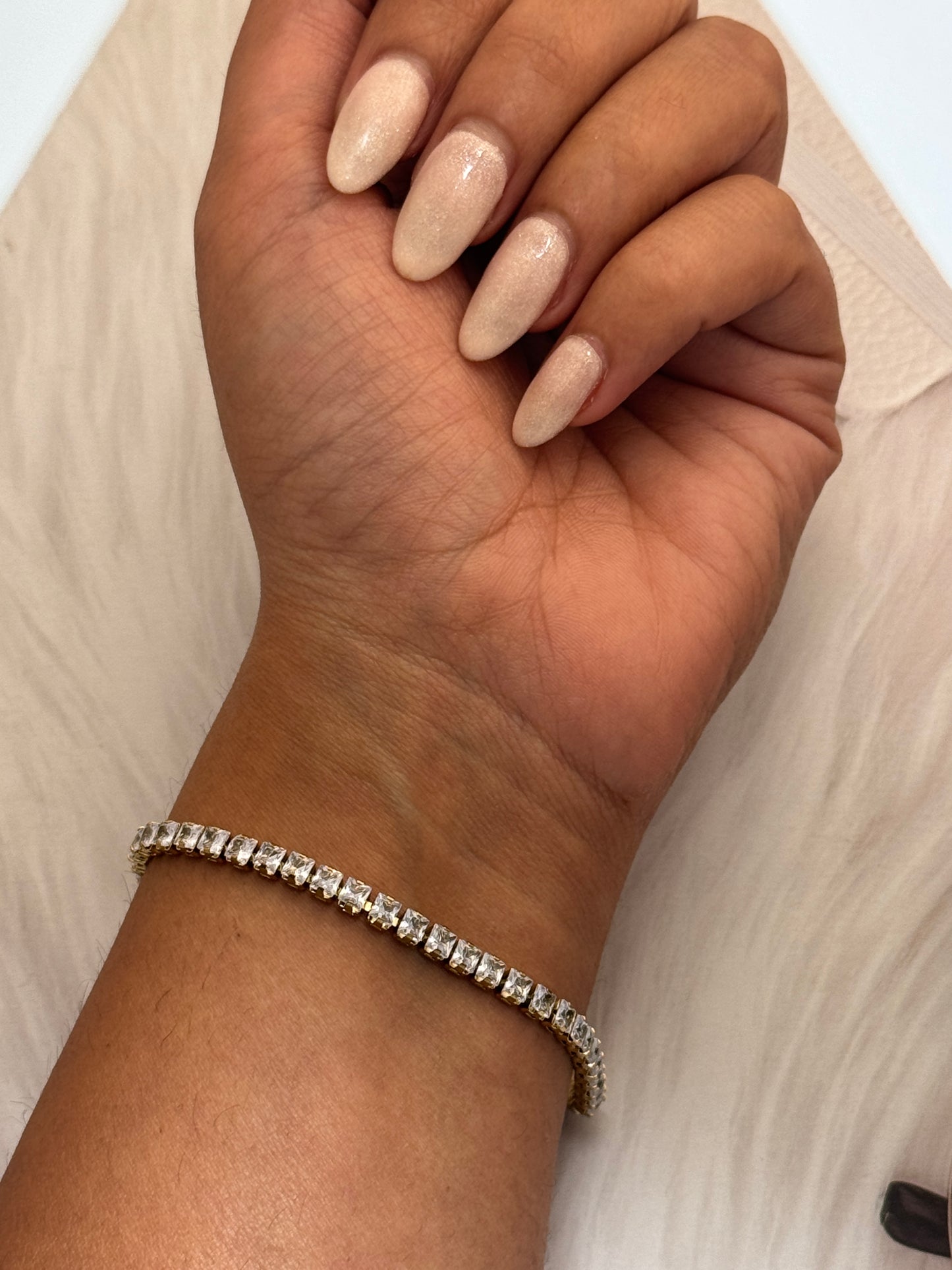 Hand wearing a silver bracelet on a neutral background