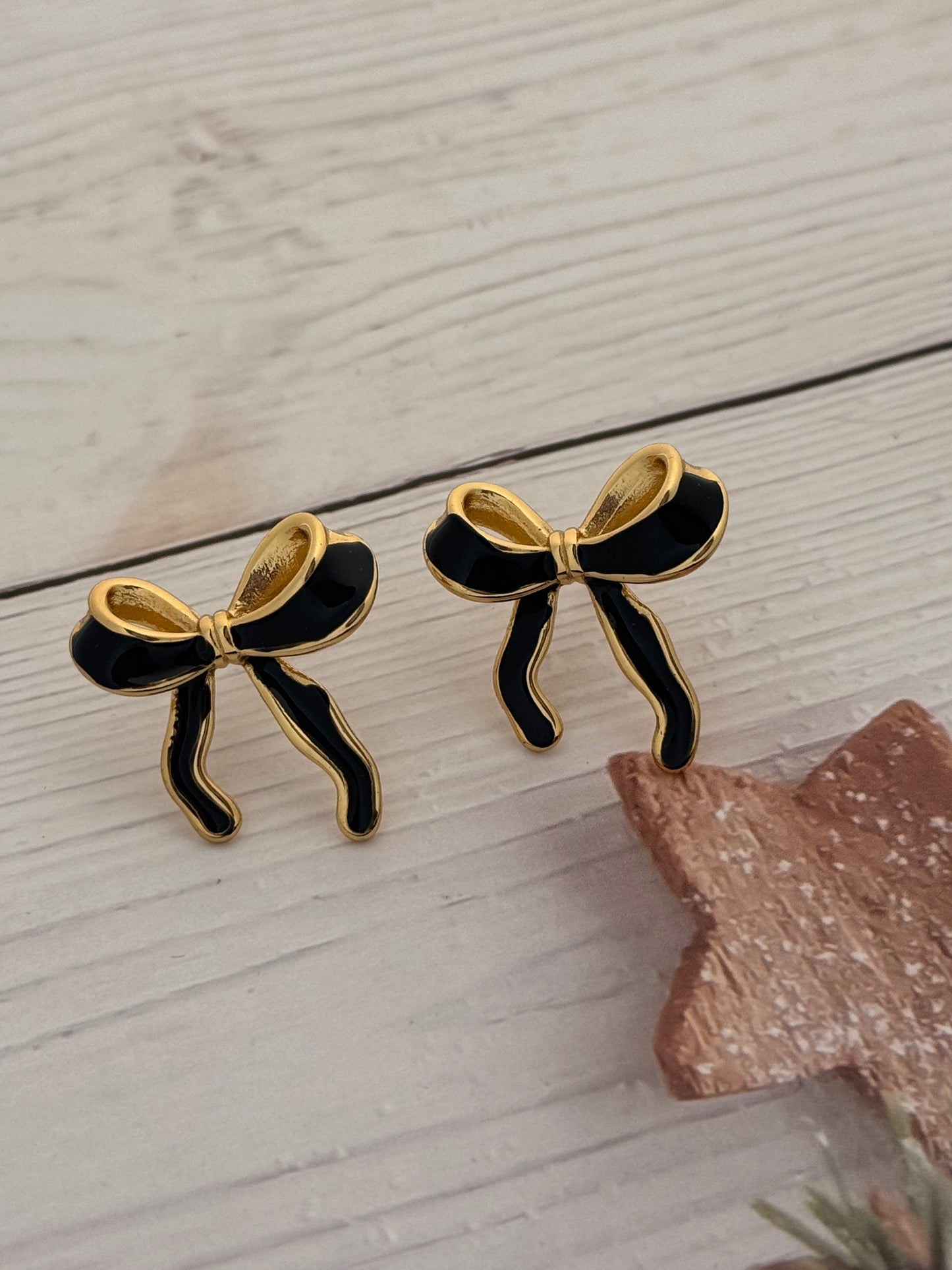 Pair of black and gold bow-shaped earrings on a light wooden surface.