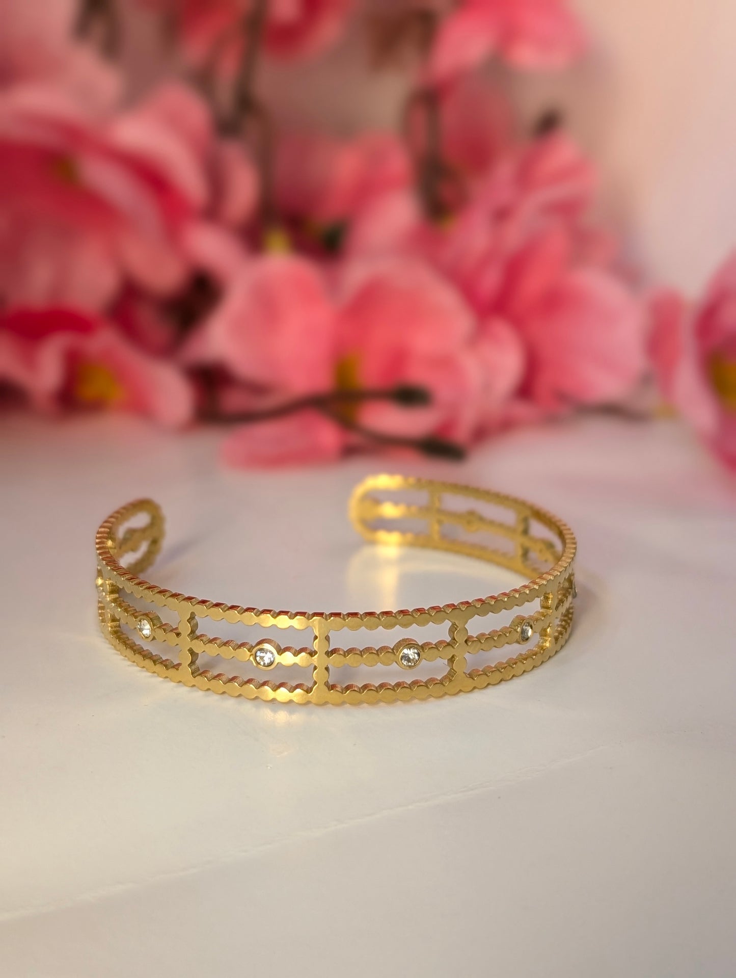 Gold bracelet on a white surface with pink flowers in the background