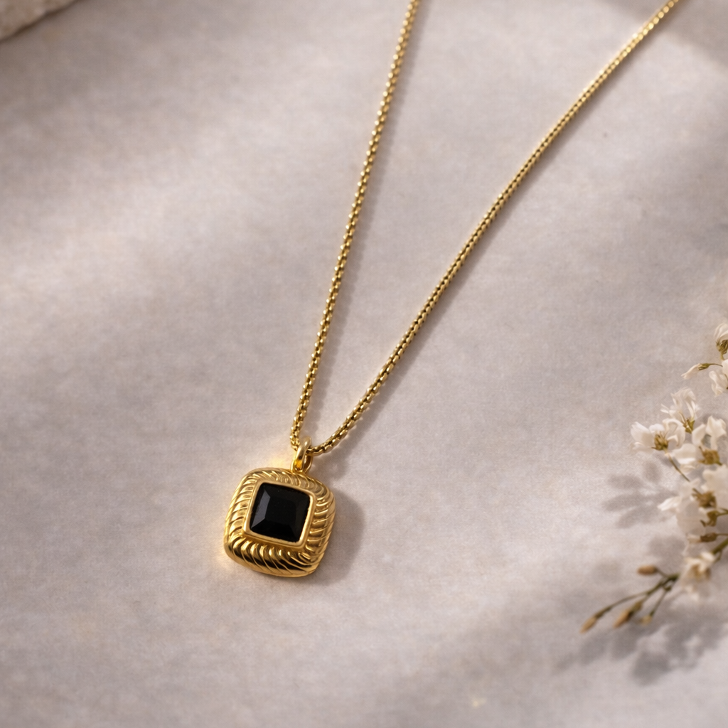 Gold necklace with a black pendant on a light background