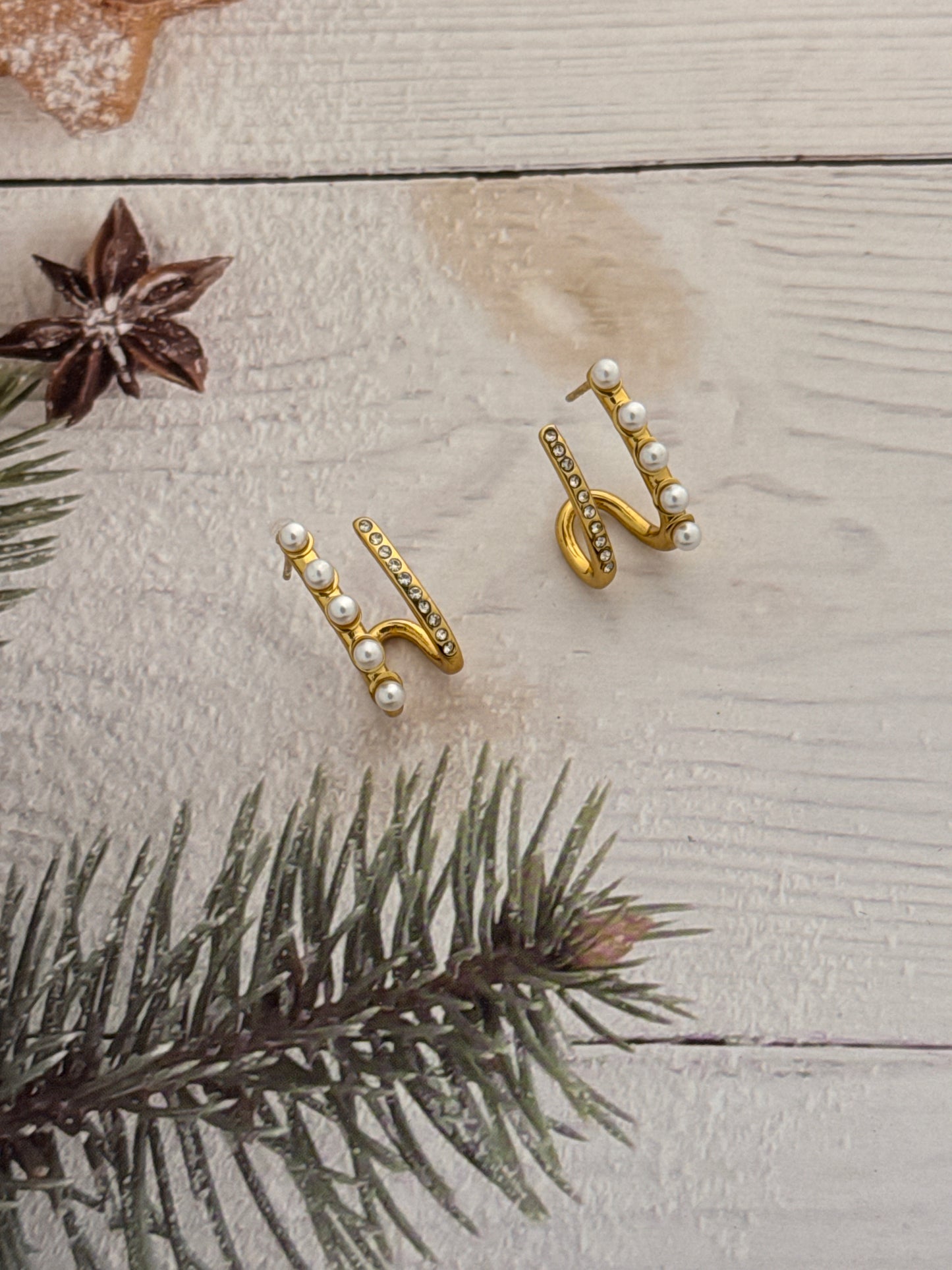 Gold earrings with pearls on a wooden surface with a pine branch and star anise.