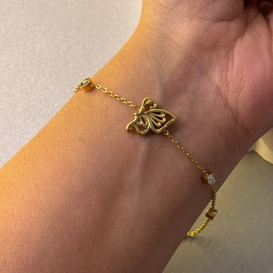 Gold bracelet with a butterfly design on a wrist against a neutral background