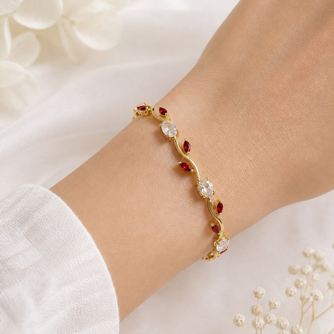 Gold bracelet with red and clear stones on a wrist against a white floral background