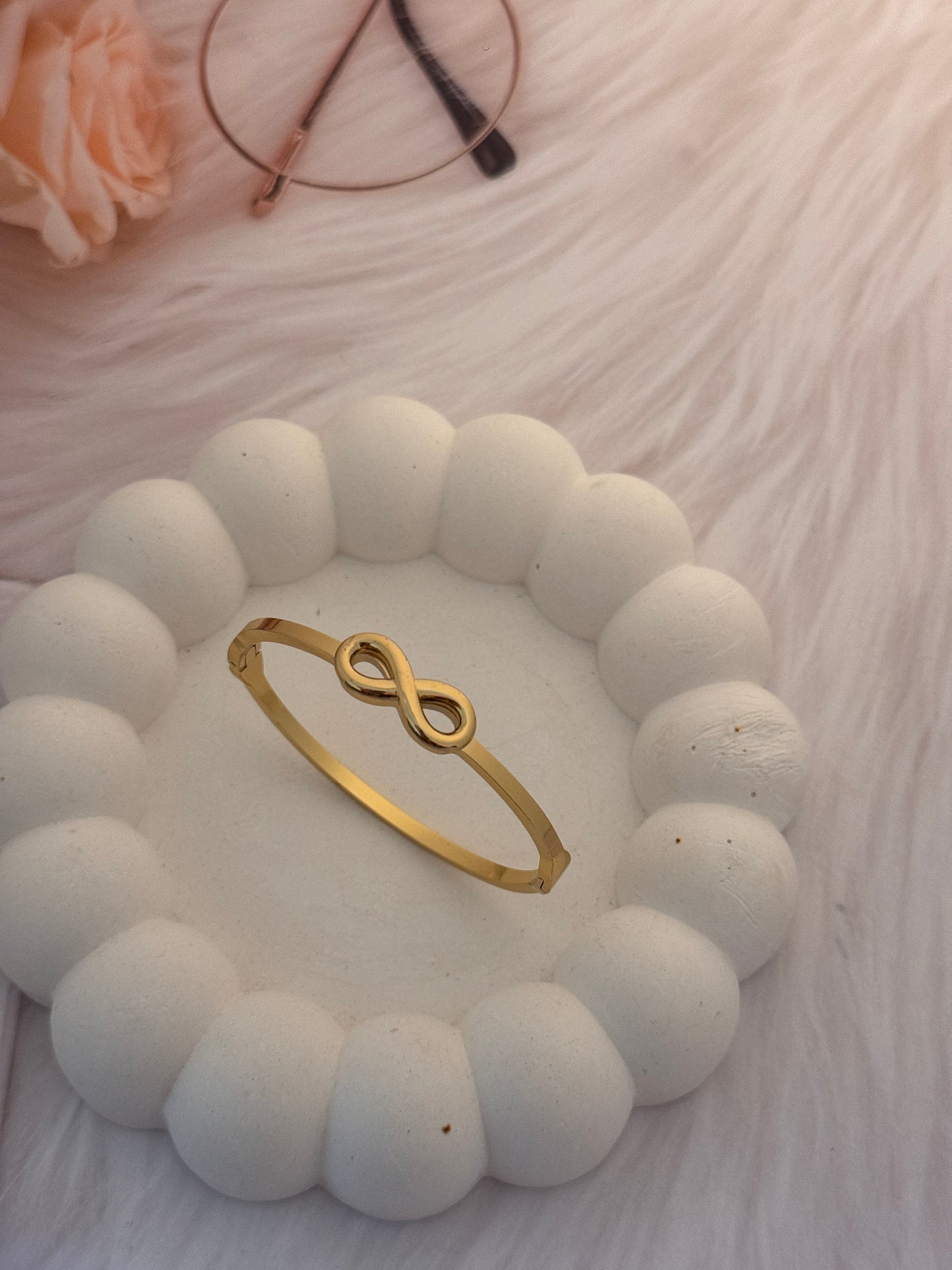 Gold infinity ring on a white stone surface with a blurred background