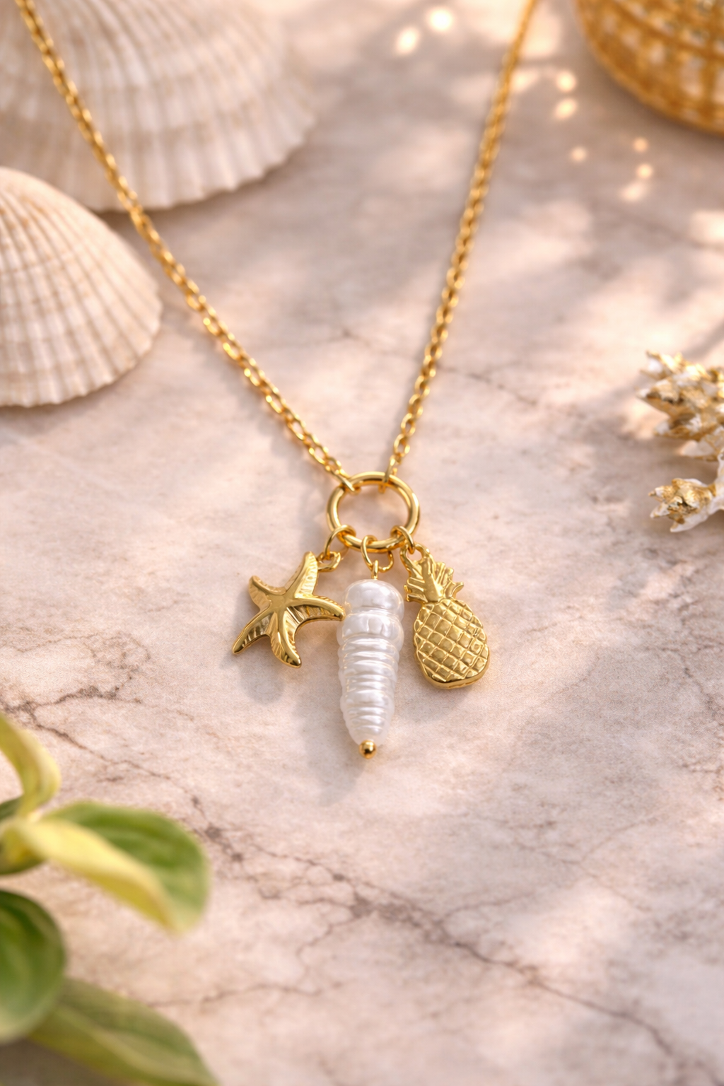 Gold necklace with charms on a marble surface with shells and plants.