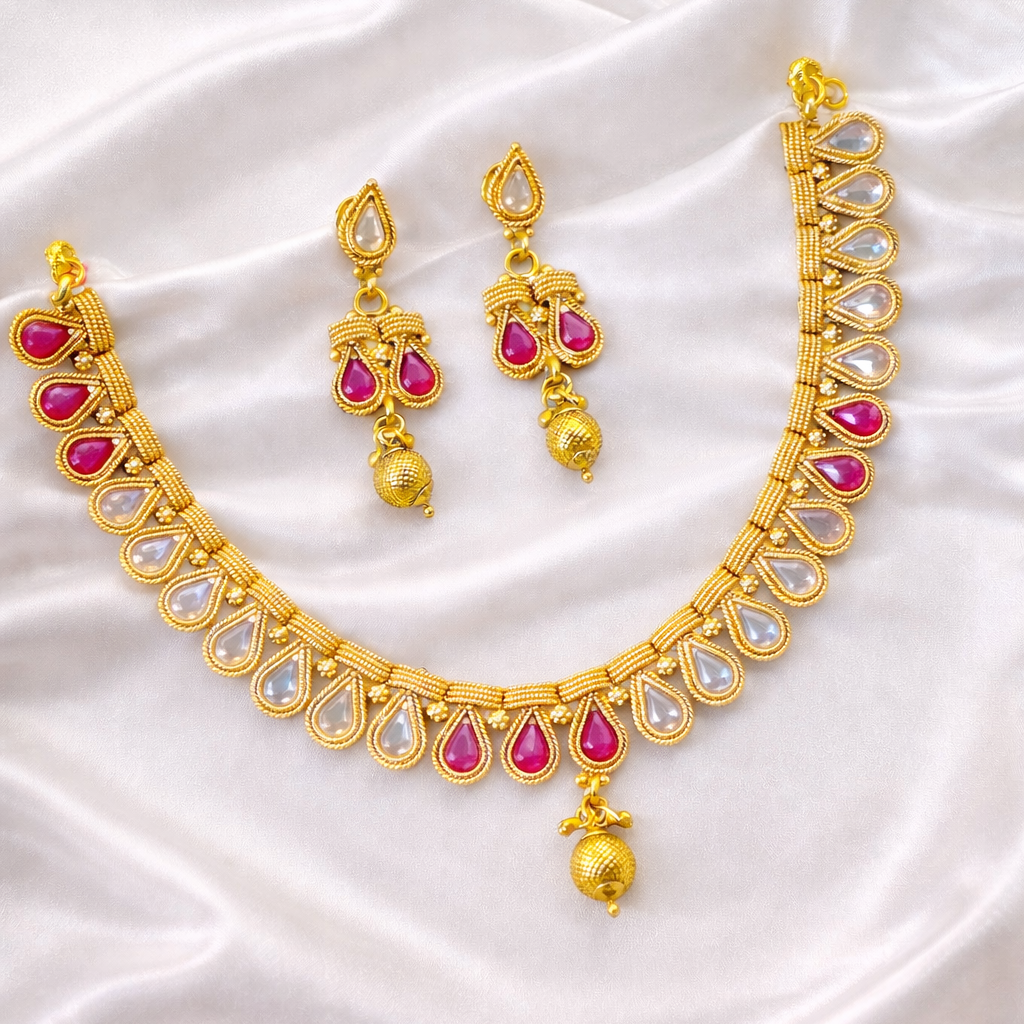 Gold necklace with pink stones and matching earrings on a white fabric background