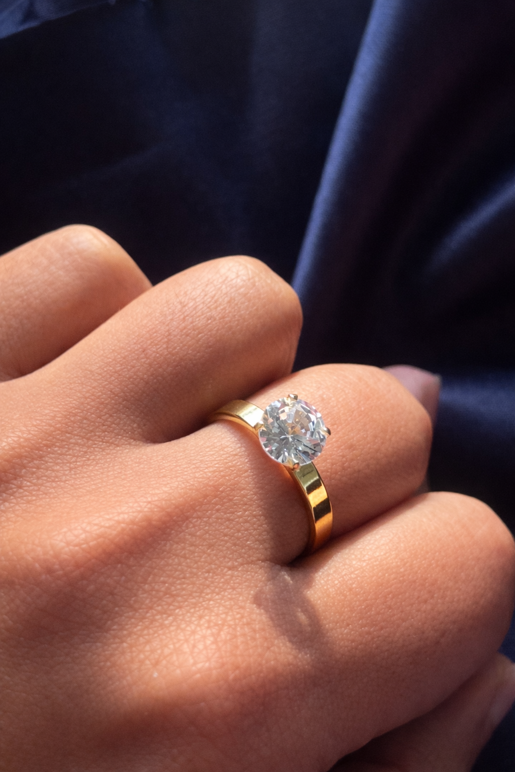 Gold ring with a diamond on a person's finger against a dark background