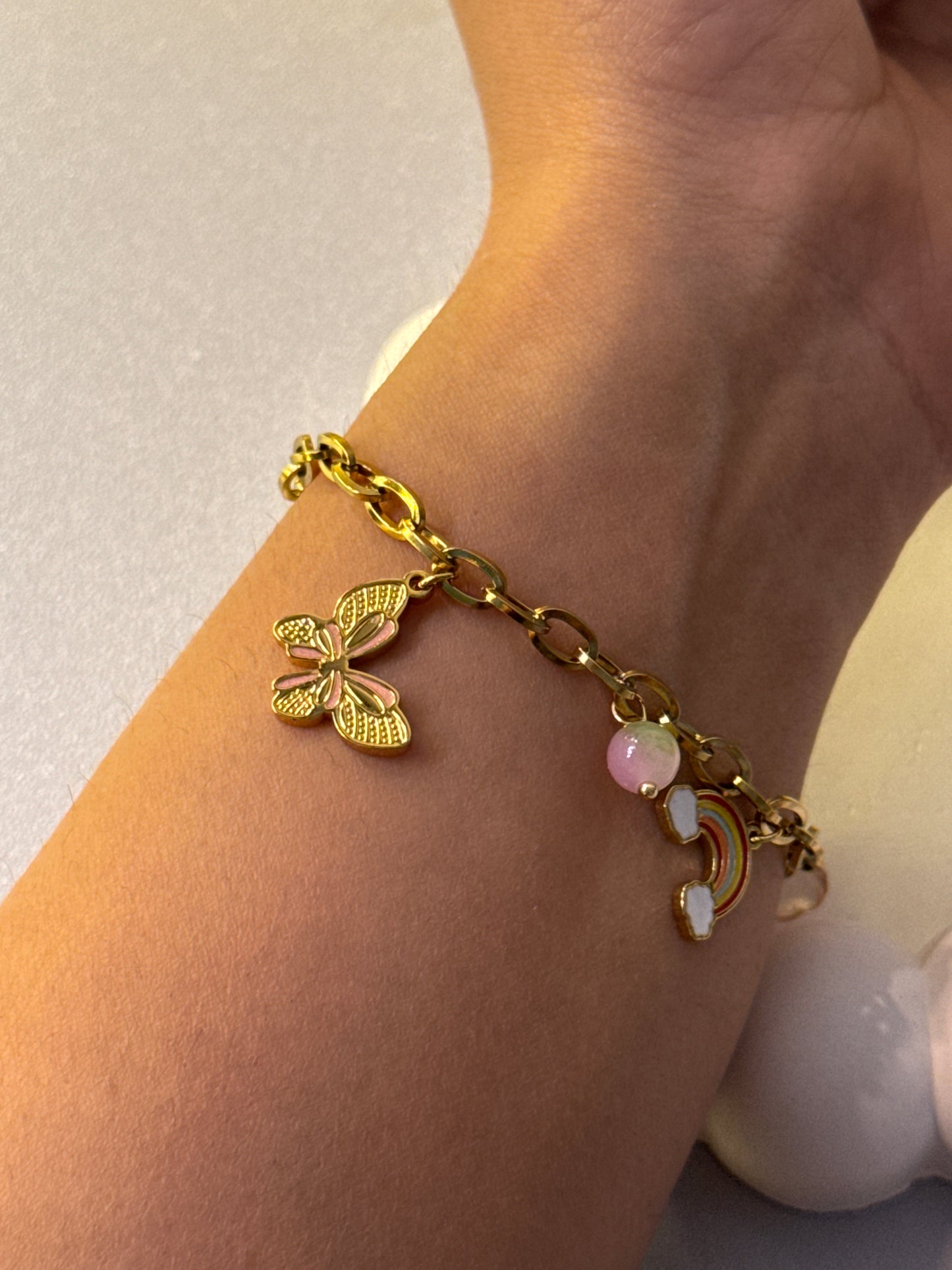 Gold bracelet with butterfly charm on a wrist against a neutral background